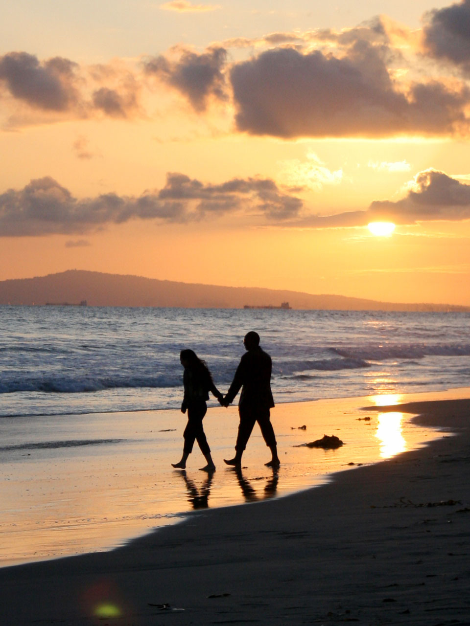 A couple strolls along Huntington Beach near sundown.
