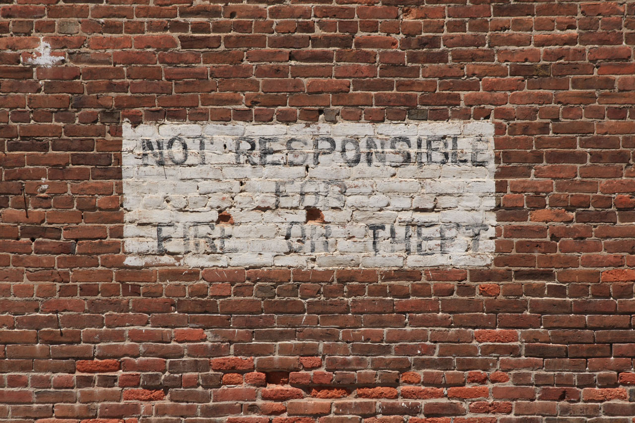 Old red brick wall with painted sign stating "Not responsible for fire or theft"