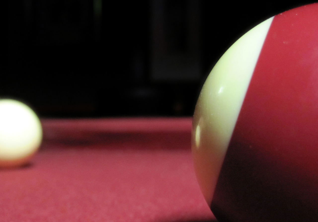 Close up of red ball on red pool table with white ball in the background
