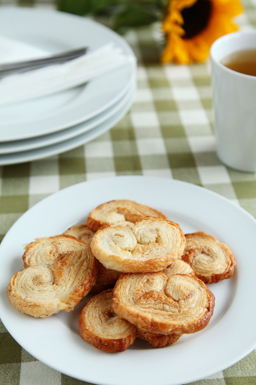 sugar and spice palmiers on plate with a cup of tea, plates and sunflower in the background