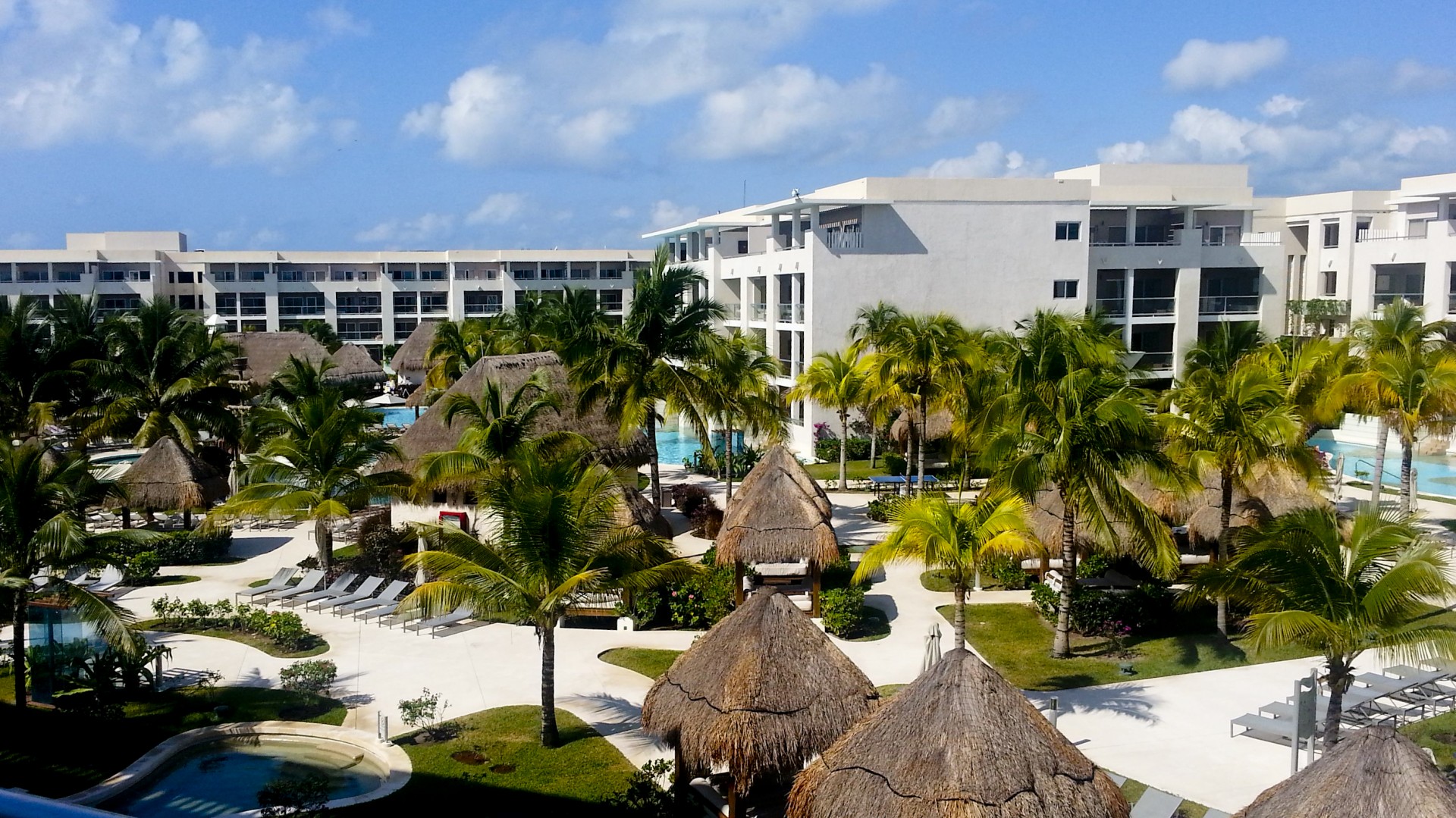 balcony view of a lush Cancun, mexico, resort complete with grass huts and many pools