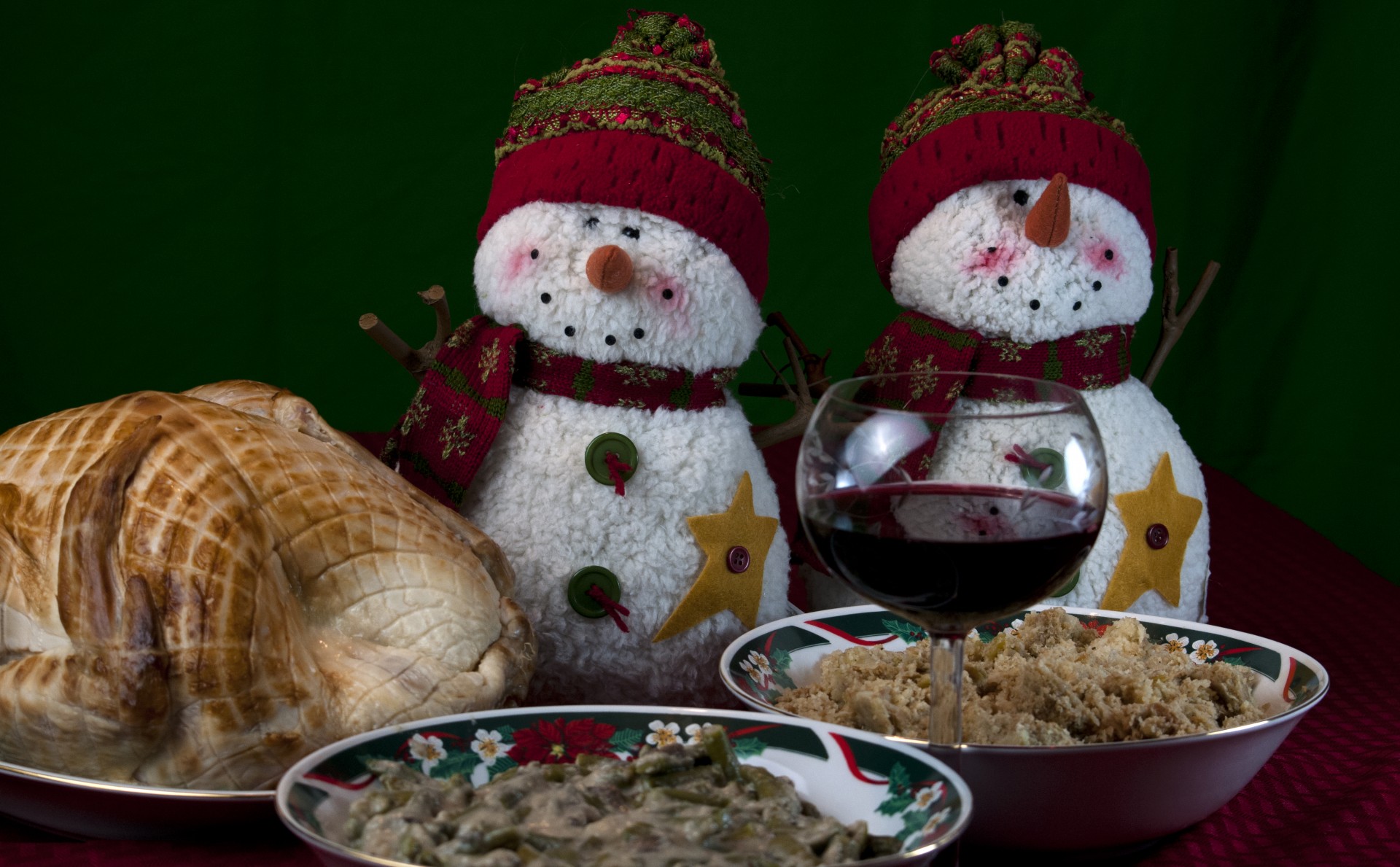Two darling snowmen decorate this table setting of a turkey, green beans, dressing and a glass of wine set in xmas china