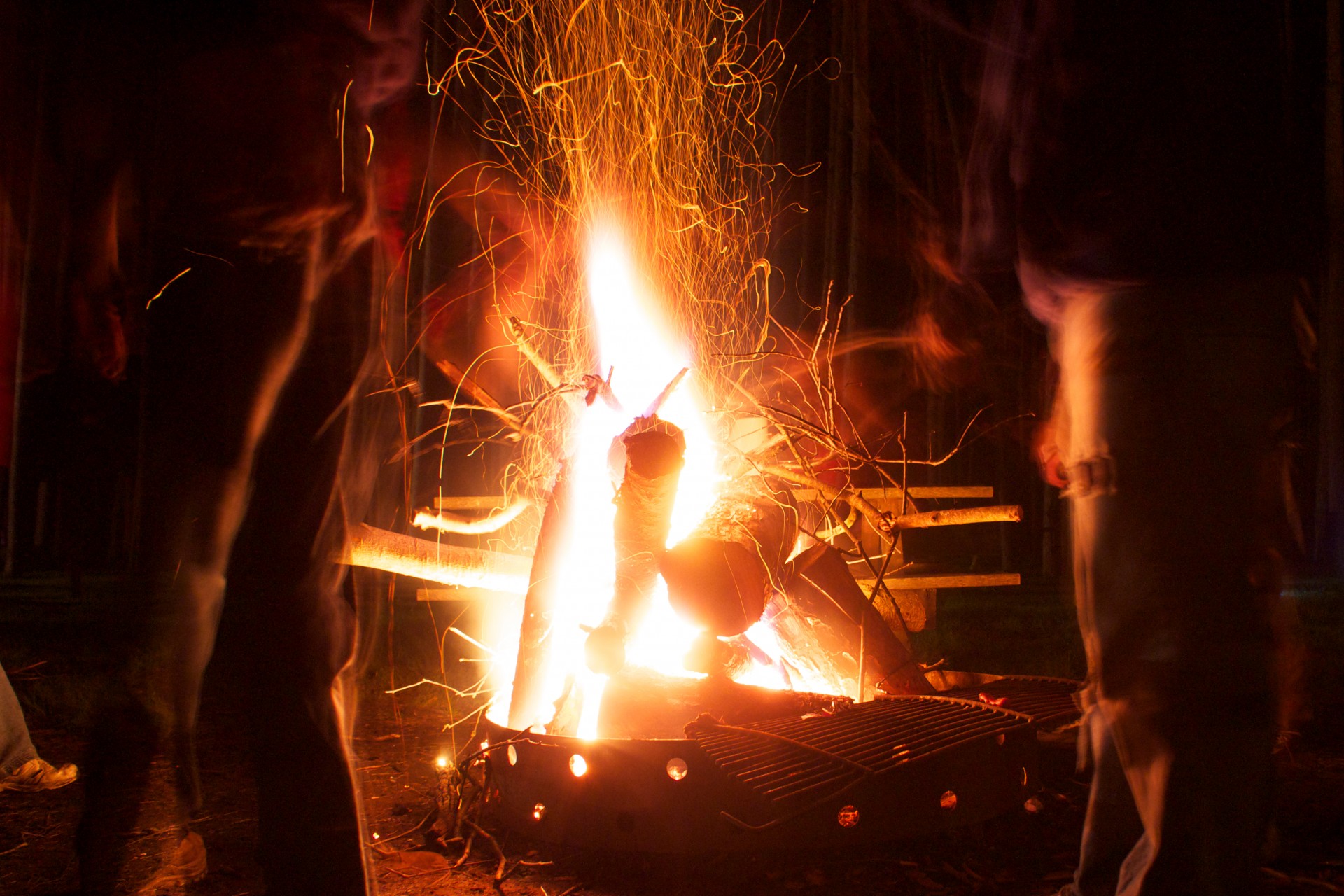 People mill around a raging campfire late at night.