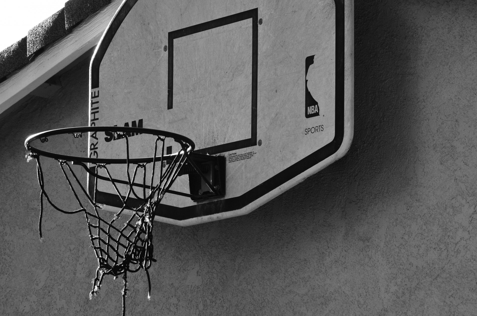 A basketball hoop  hooked above a garage with torn net.  A hoop that has seen many hours of play