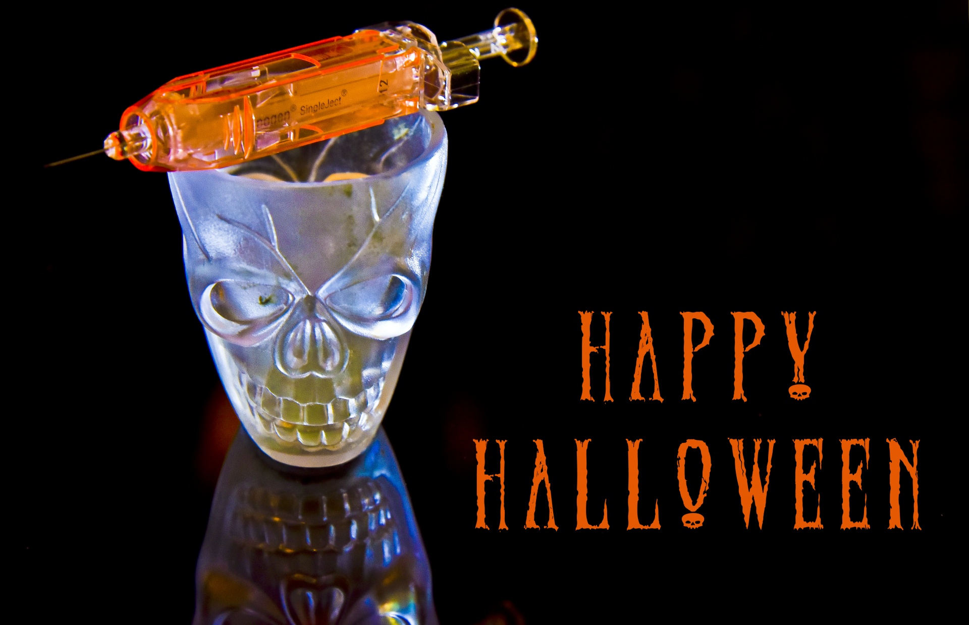 Skull shotglass and hypodermic needle against a black background Happy Halloween greeting
