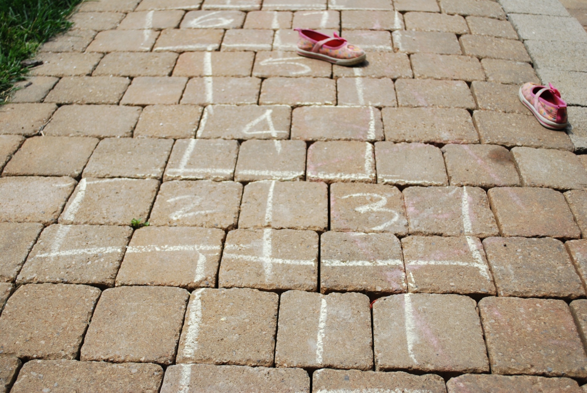 Hop scotch game drawn on cobble stone sidewalk with children's shoes