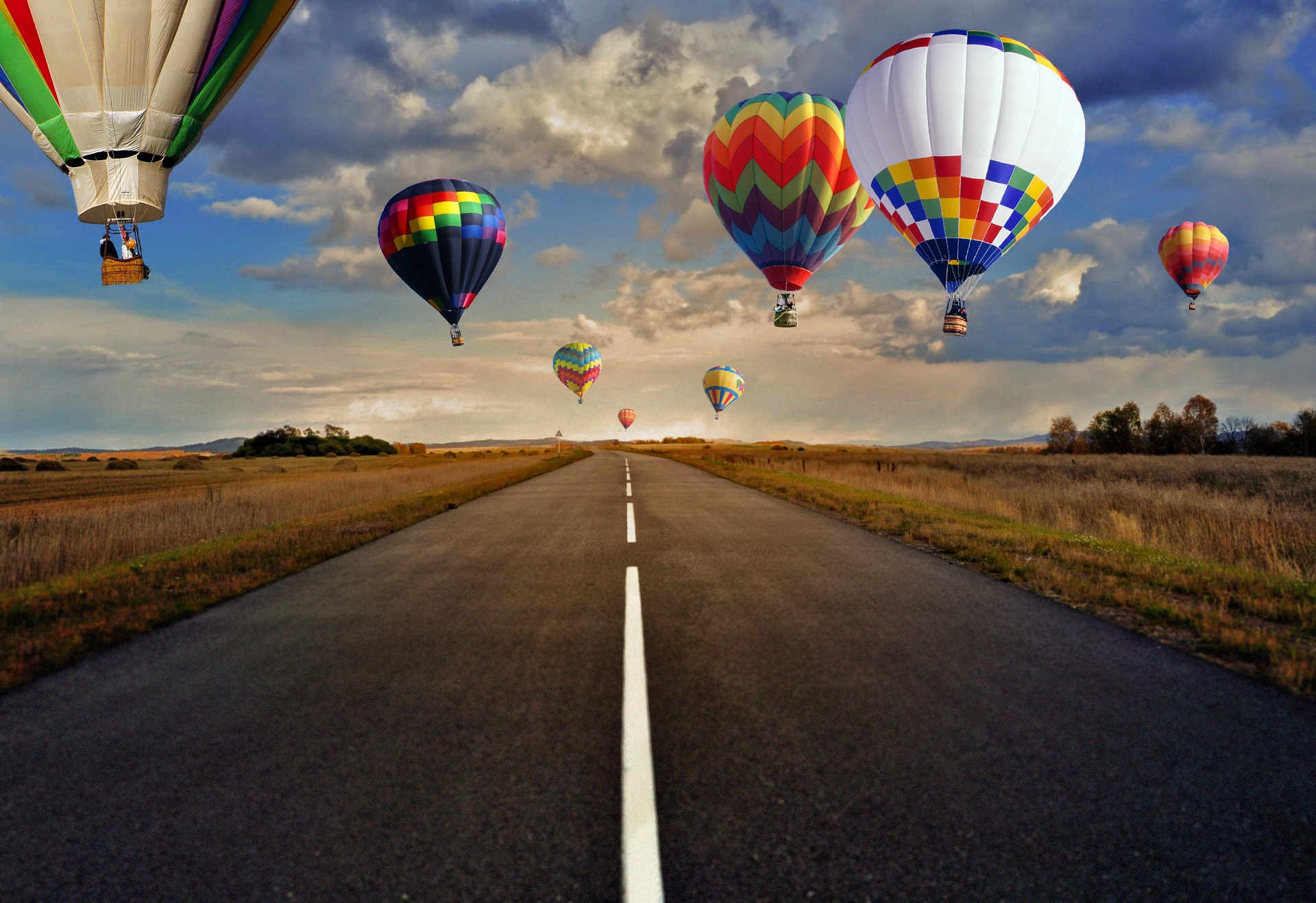 A road less traveled, unless by balloon. Various hot air balloons floating above a road through open spaces