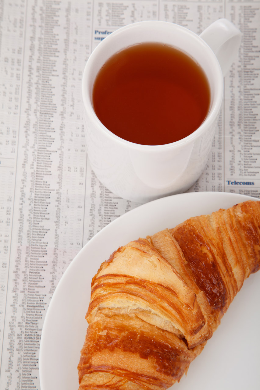 cup of tea and a croissant on a plate on newspaper with market data