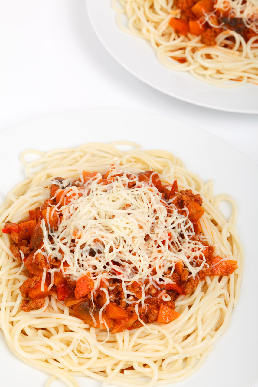 spaghetti bolognese on plates with cheese on top on white background