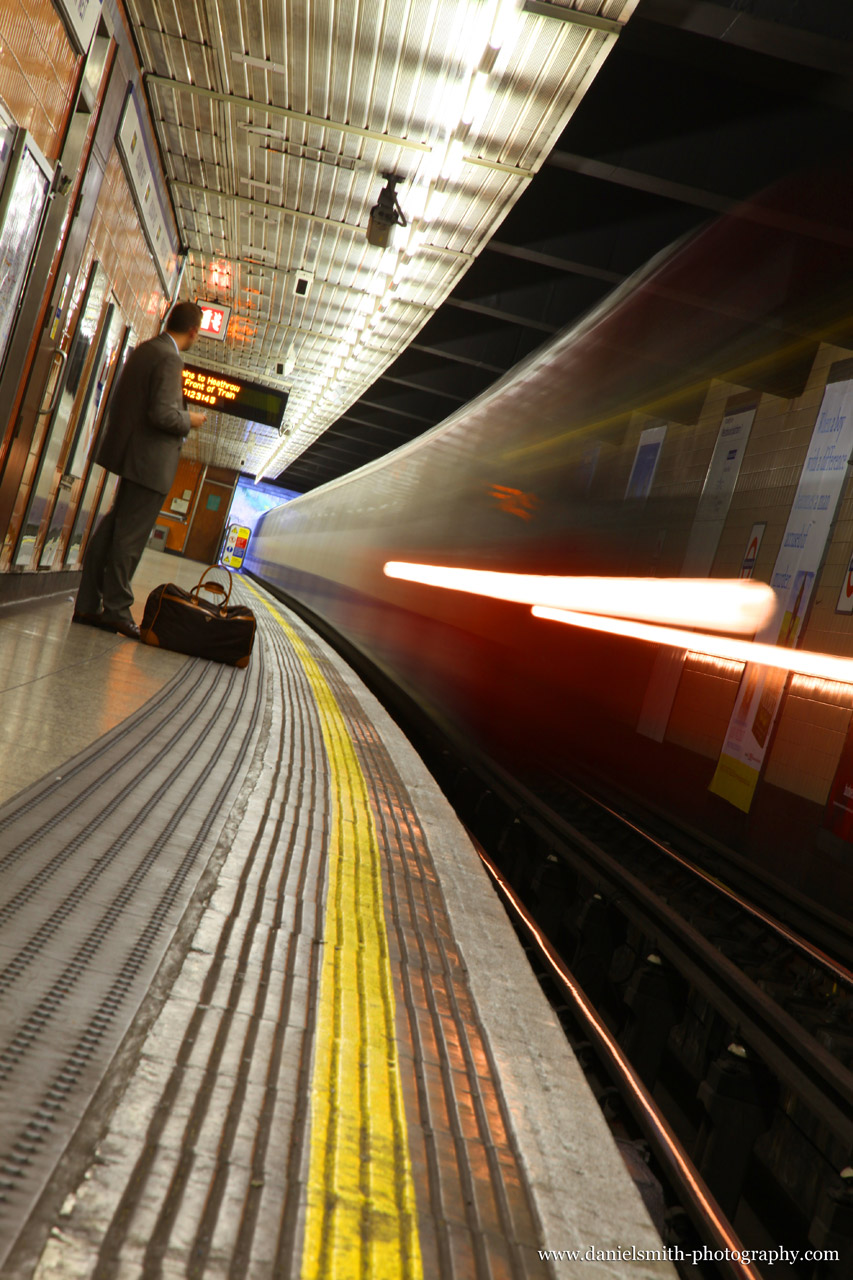 A train pulling up to the platform in the London Underground with man standing on platform.