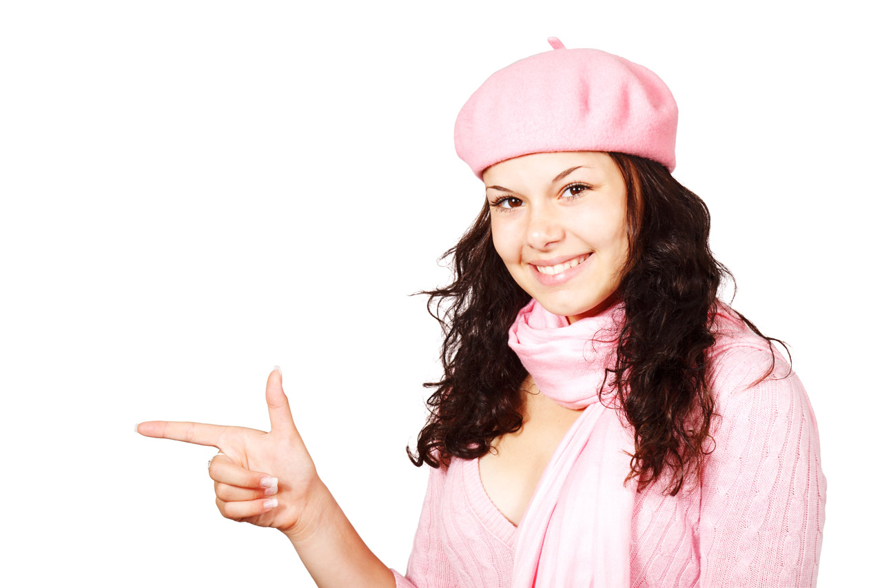 young woman in winter pink pointing her finger at something isolated on white background