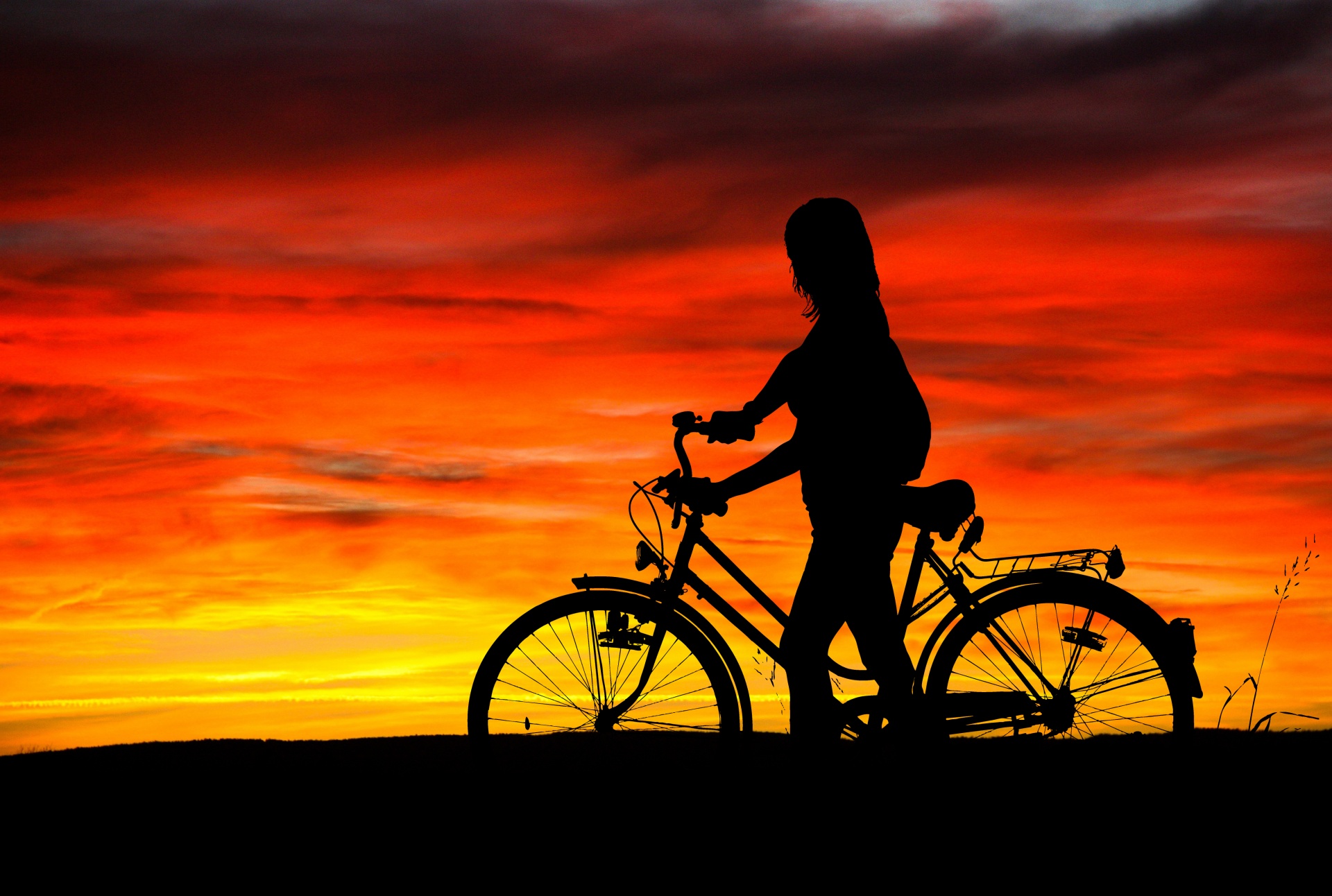 Black silhouette of girl pushing her bicycle at sunset