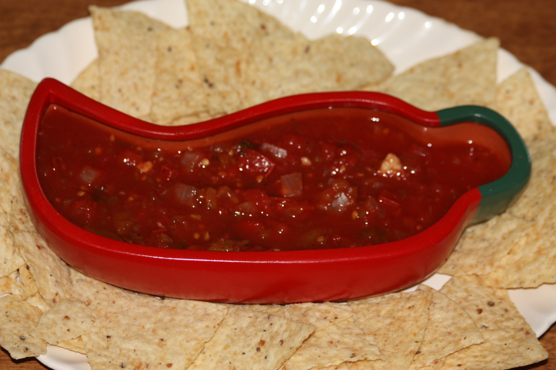 Home made picante sauce in a red chili pepper bowl, surrounded by chips, on a platter.
