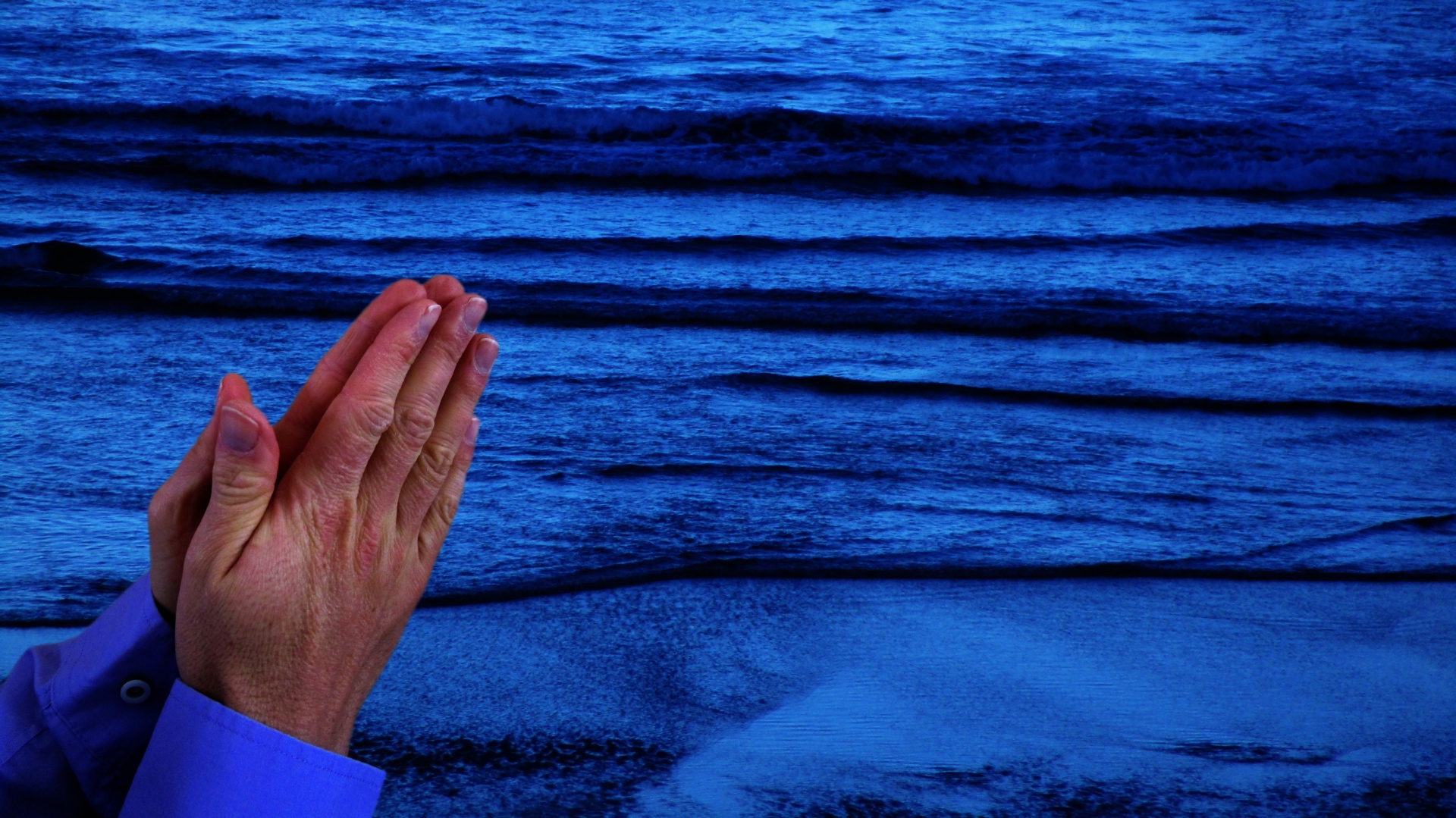 Praying hands with dark blue sea in the background.