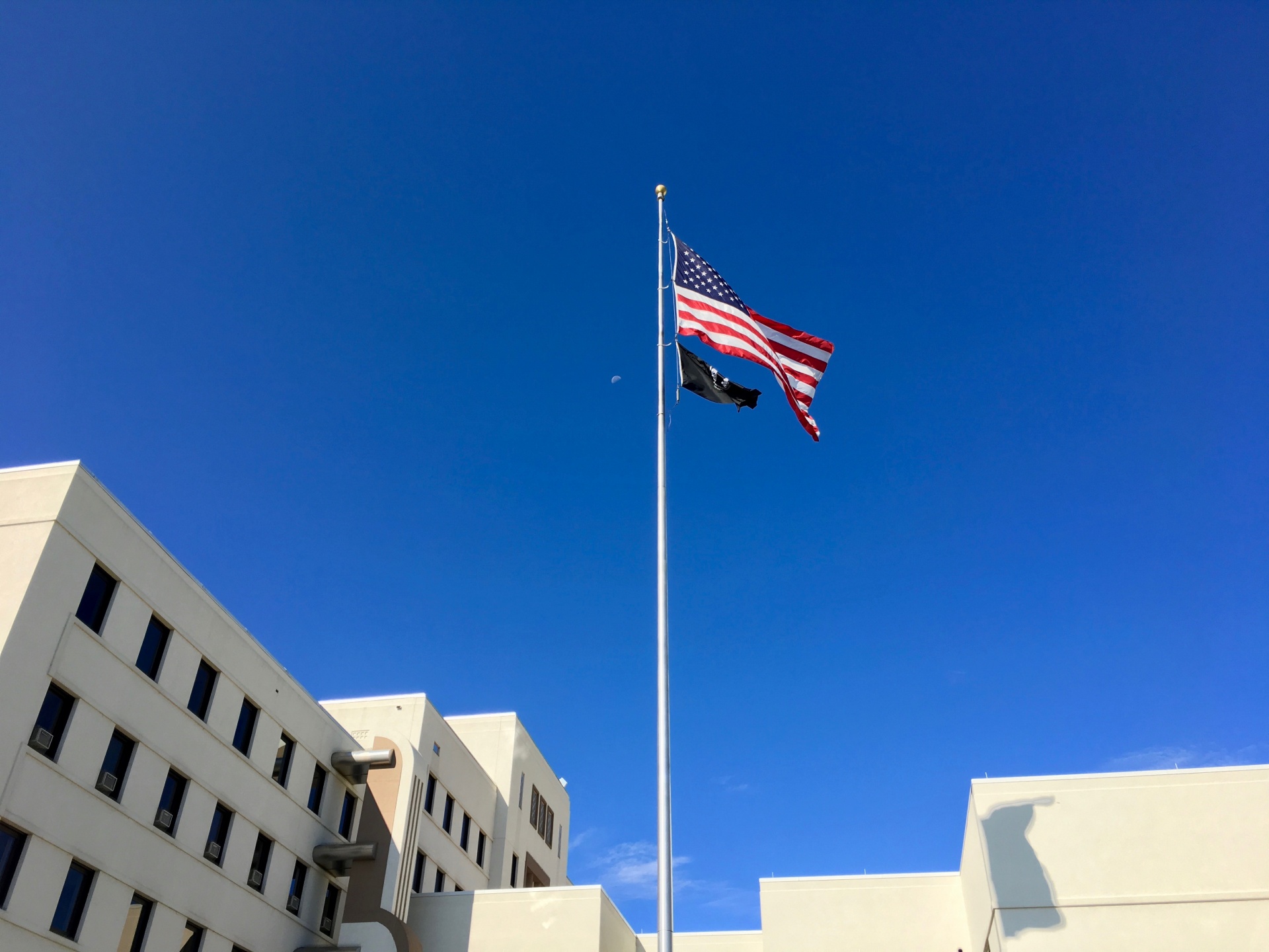 The US Flag and the POW Flag fly in front of the Grand Junction VA Medical Center. The Moon is visible in the BG behind the flags.