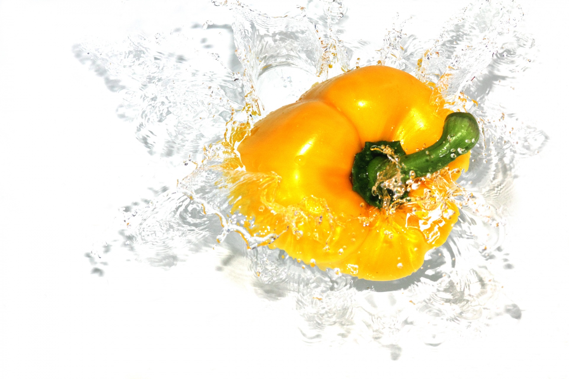 A yellow bell pepper, splashing into water.