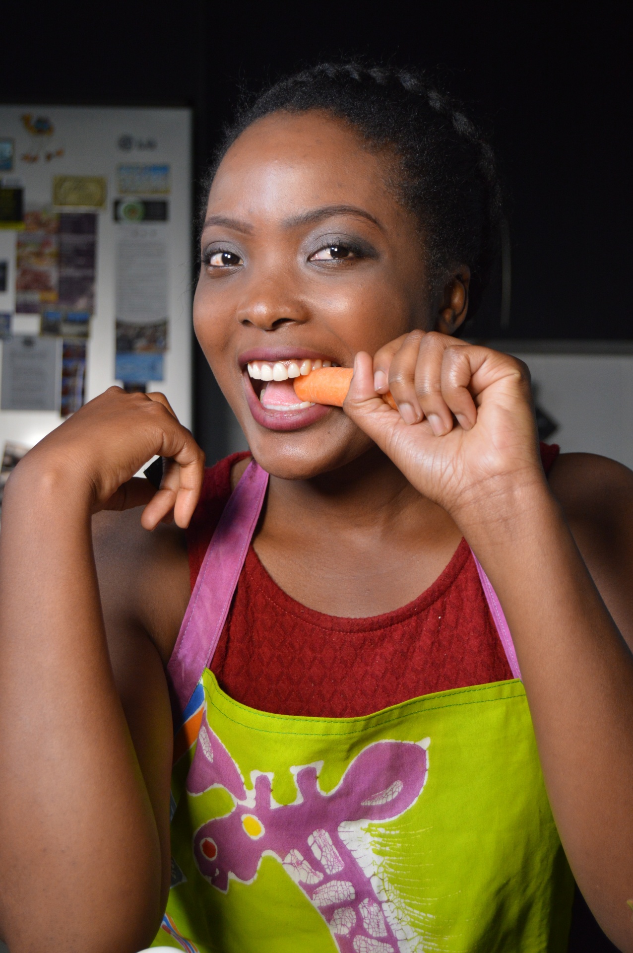 An image of a beautiful African lady biting a carrot in the kitchen