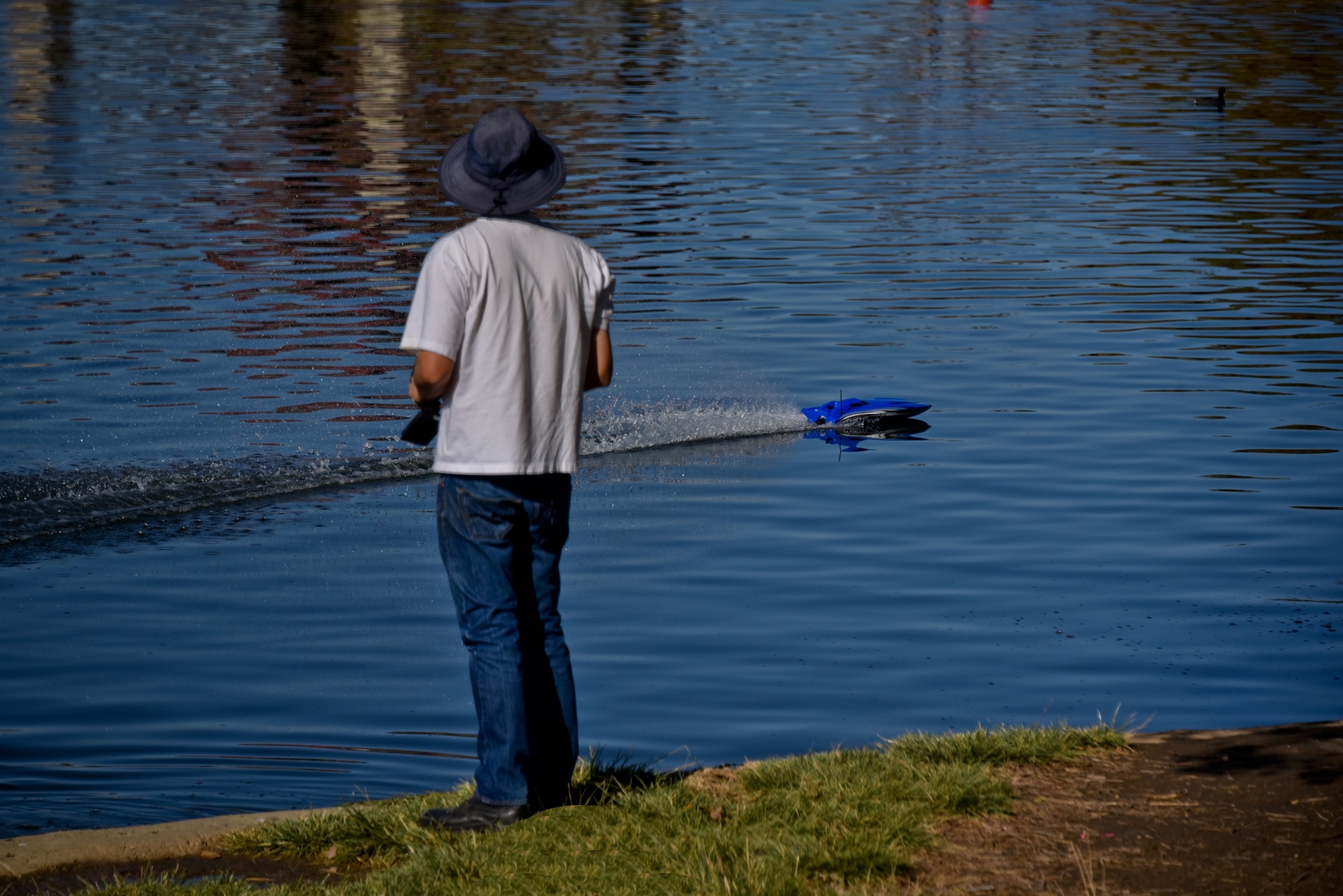 Man wearing a hat controlling a radio controlled boat on the water of a lake