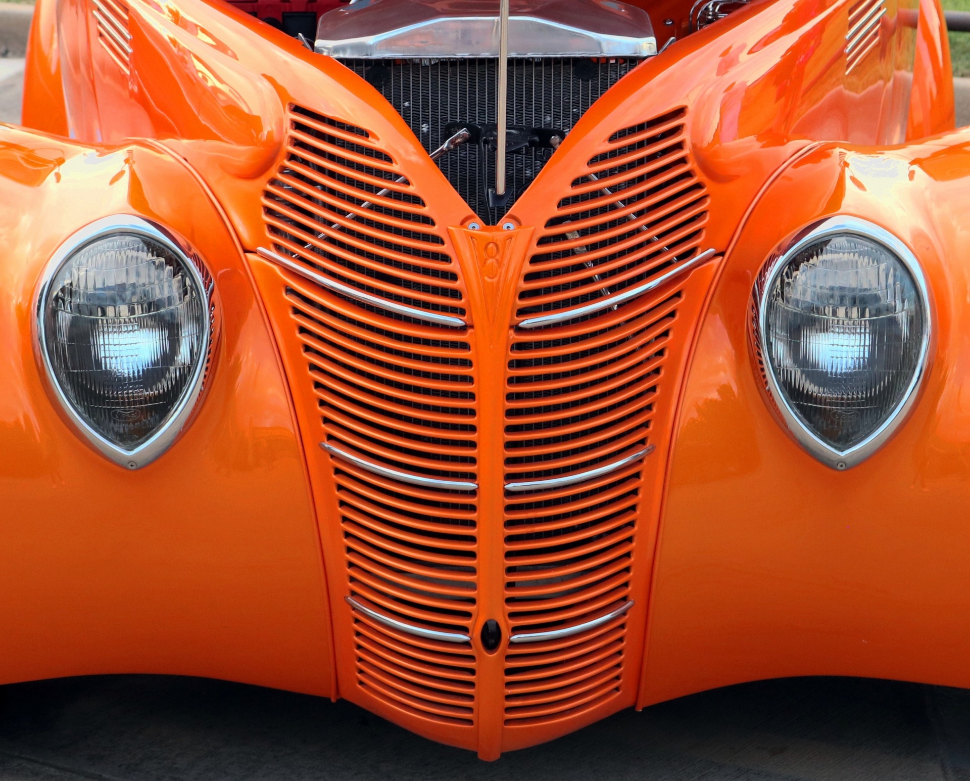 Close-up of the grill and headlights of a customized orange 1938 Ford coupe classic car.