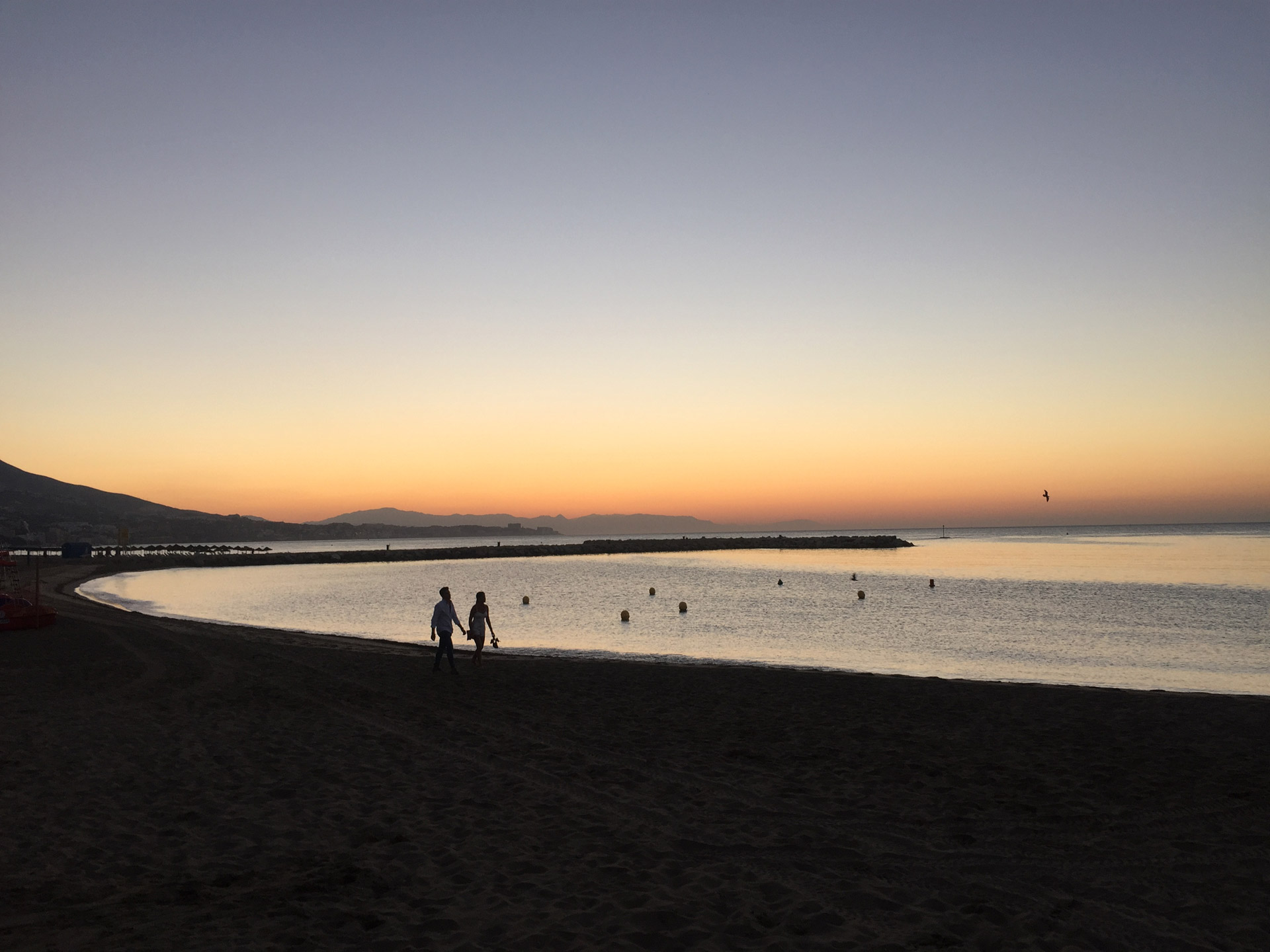 A couple walking on a beach in Fuengirola at sunrise.