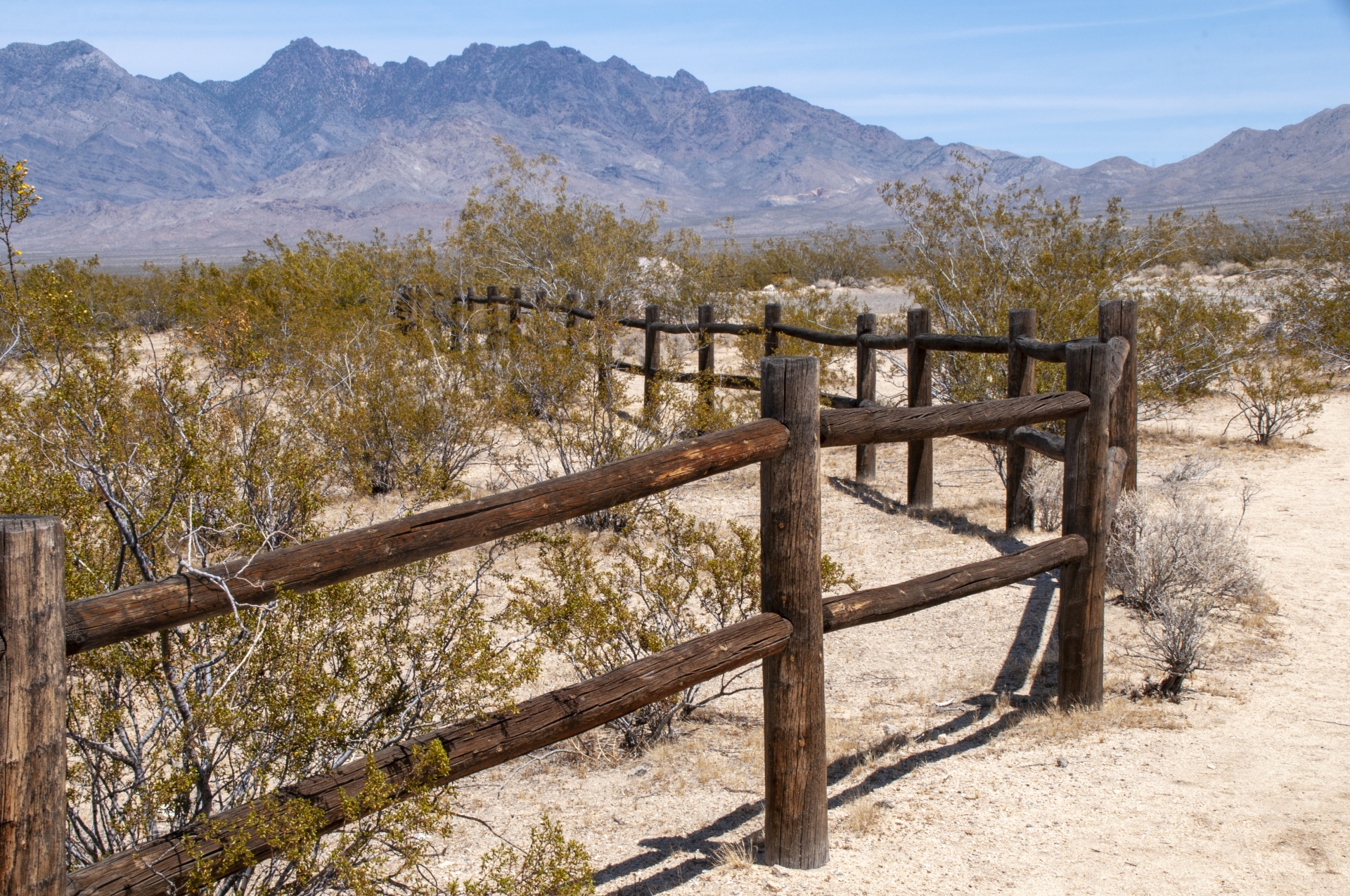 A wooden fence in desert with brush all around it