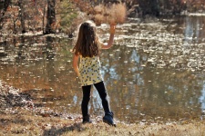Little Girl Throwing Leaf In Pond