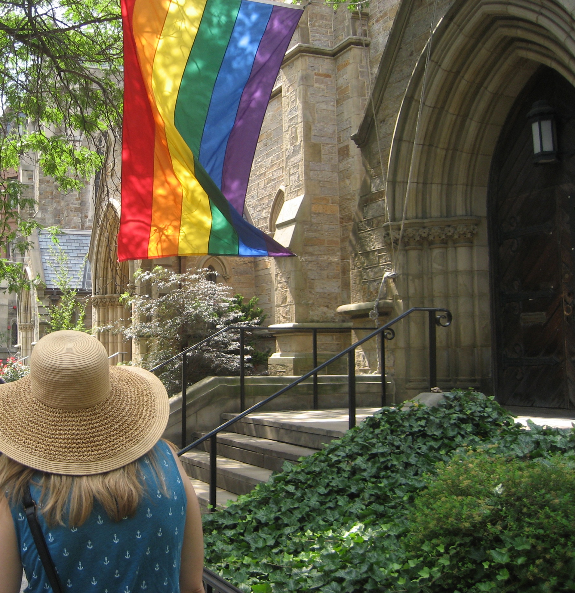 Woman in hat walking up to church doors with rainbow flag