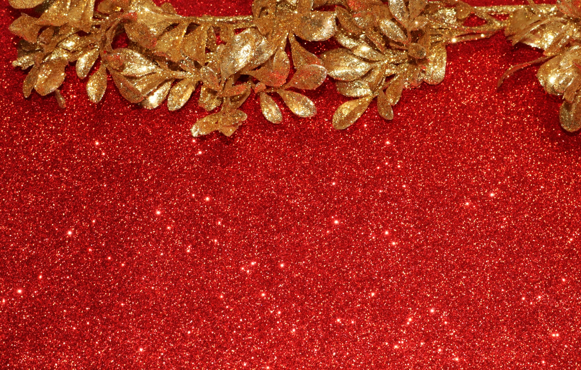 A Christmas background of a stem of gold glittery leaves on a red glitter background with room for text.