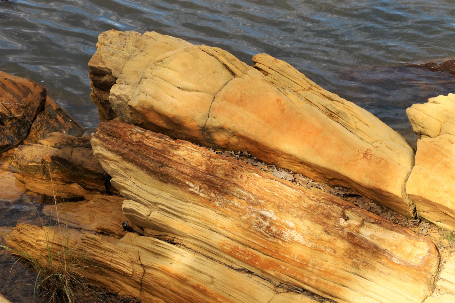 Close-up of a beautiful golden brown sandstone rock formation as it sits in the water at the edge of a lake.