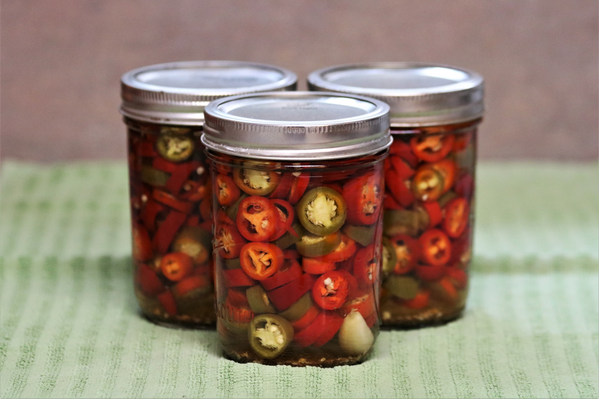 Three home-canned red and green jalapeno peppers on a green kitchen towel.