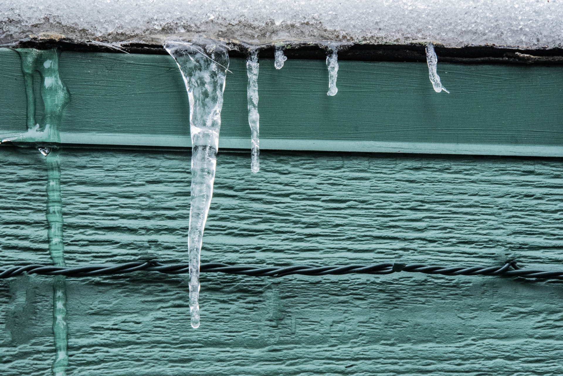 Icicle hanging from the eaves of a green building in Winter
