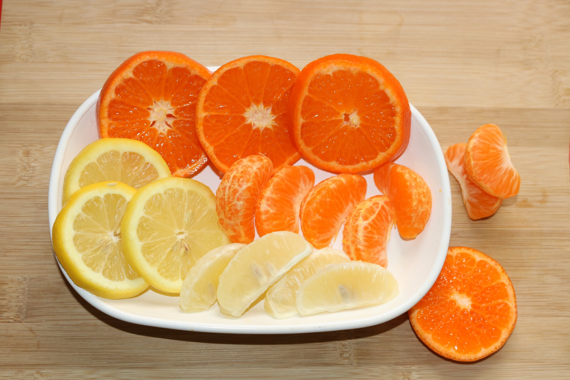 Slices and segments of oranges and lemons on a white plate with a wood background.
