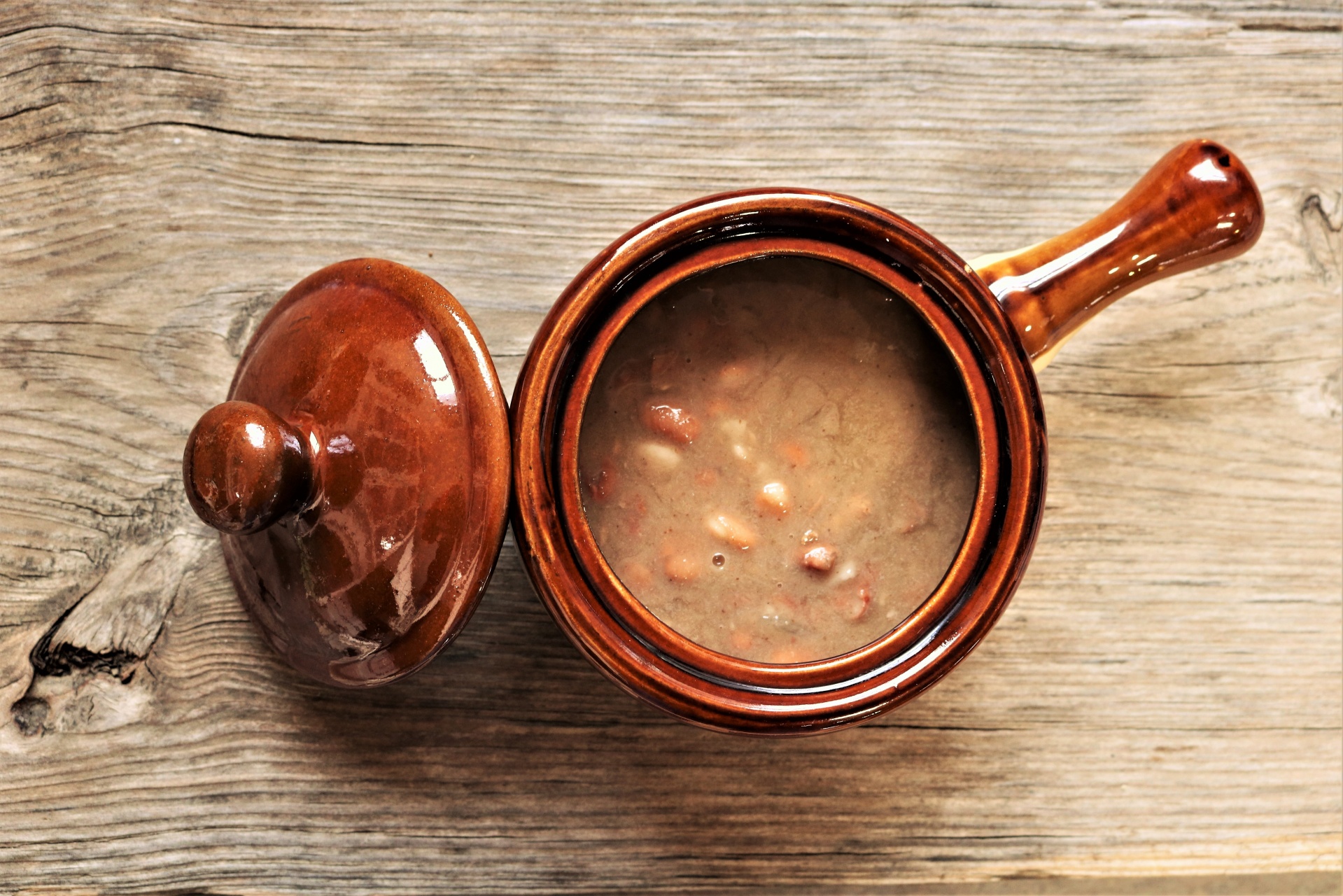 Top view of a vintage bean pot full of cooked pinto beans on a wood grain background.