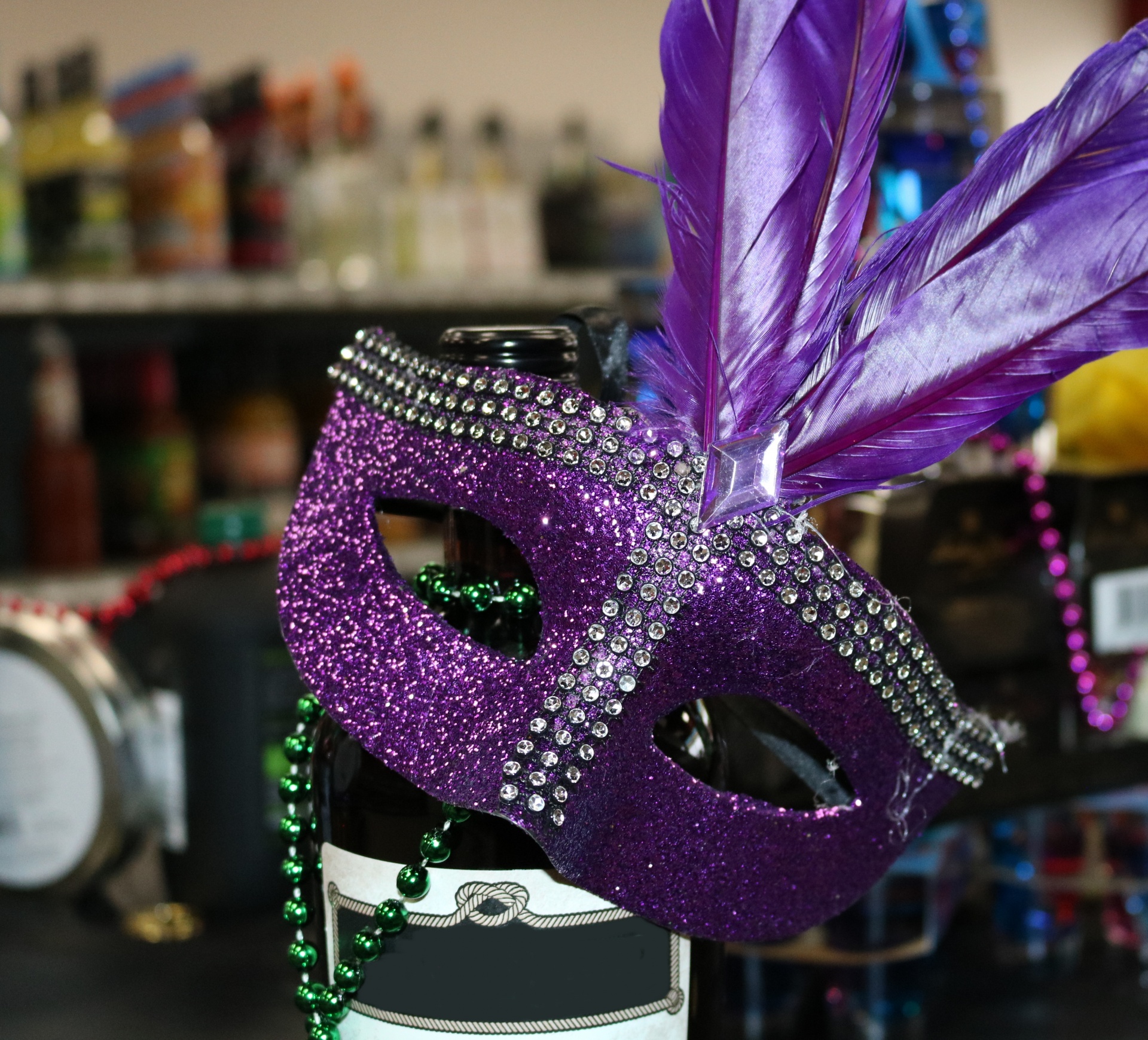 Close-up of a glittery purple Mardi Gras mask hanging on a bottle of wine inside a liquor store.
