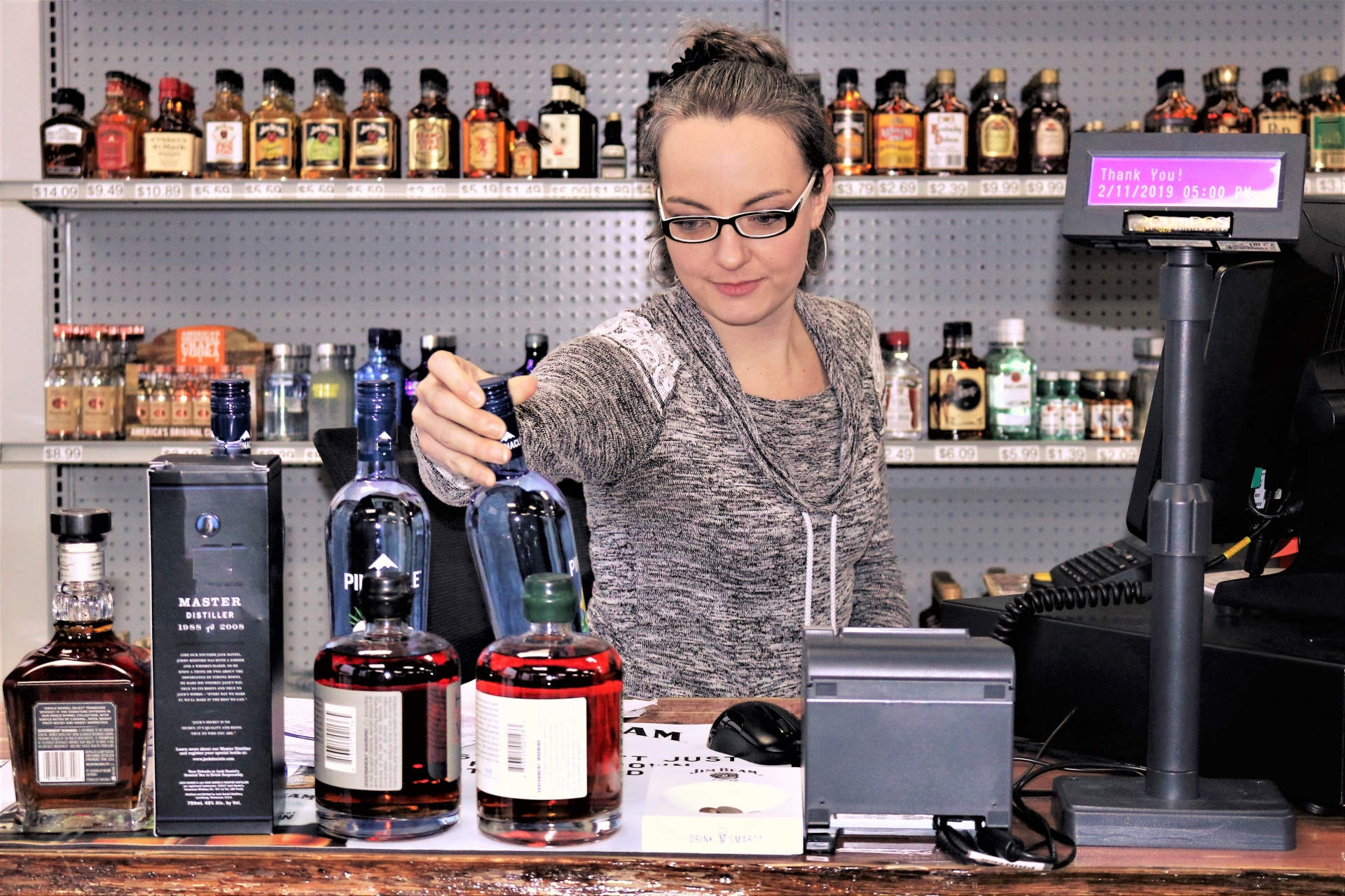 A pretty woman working behind a cash register at a liquor store.