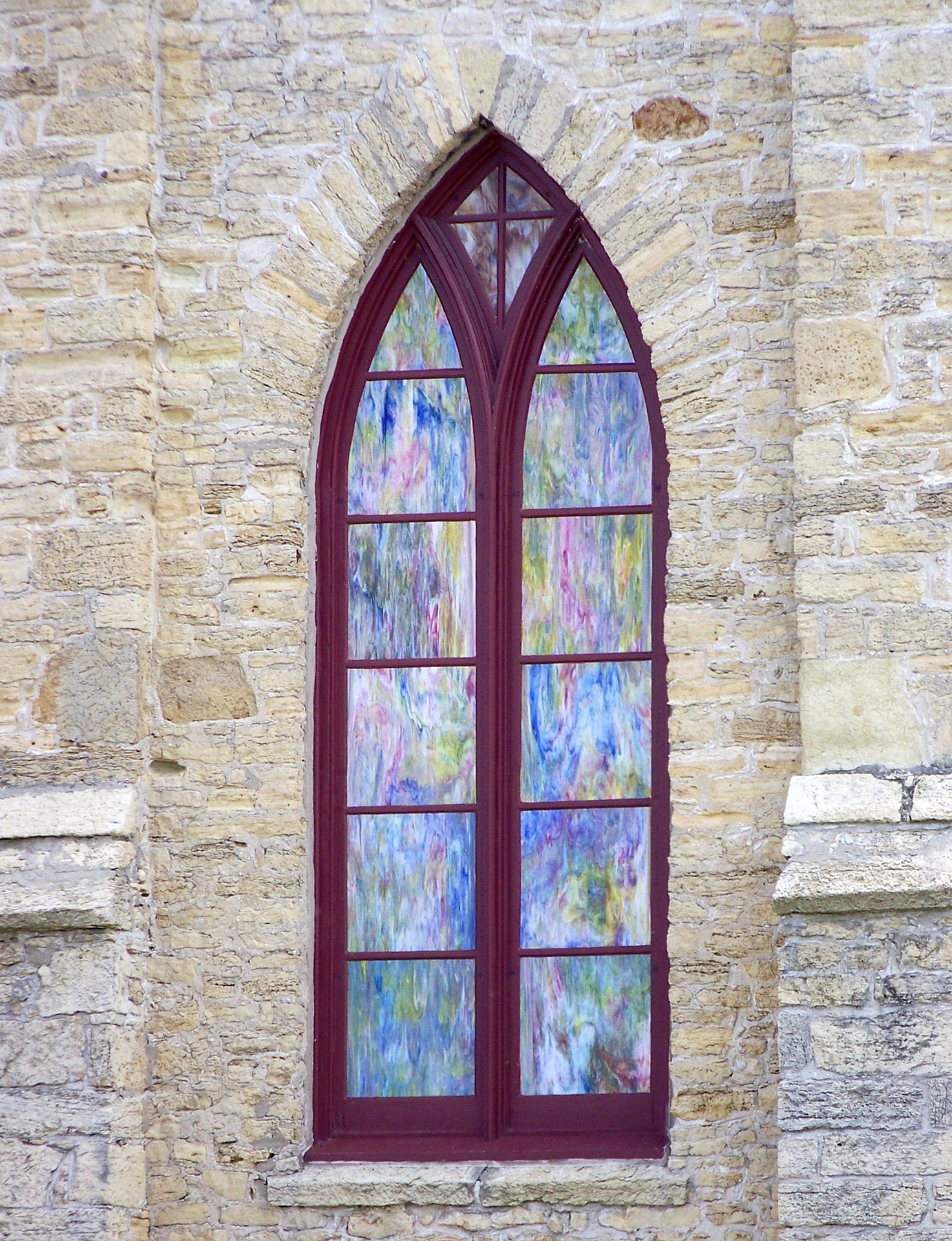 A stained glass window displays pastel colors in a stone church facade.