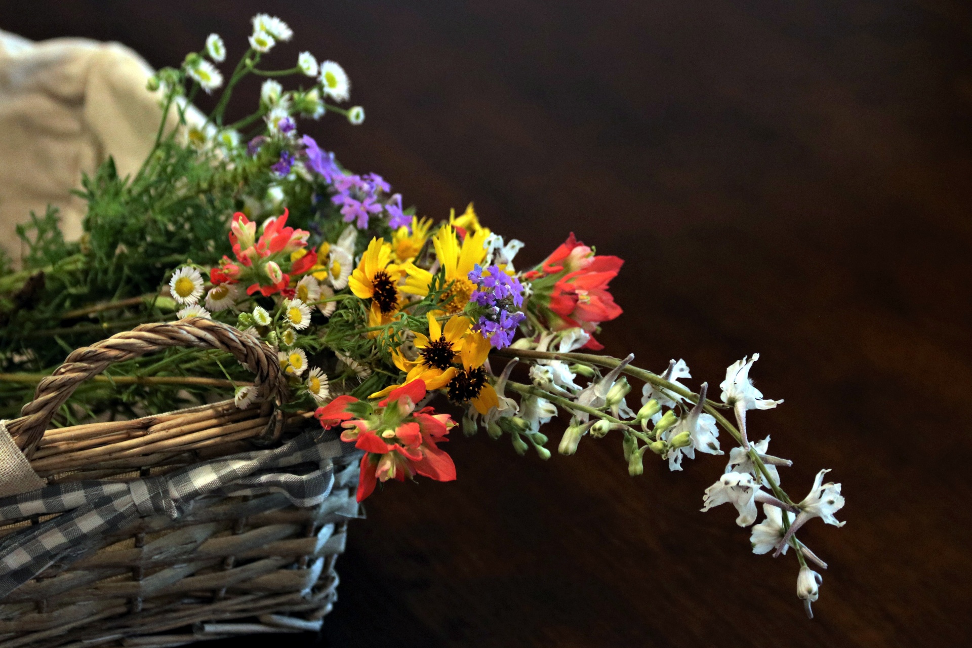 A variety of wildflowers in a wicker basket on a black background.