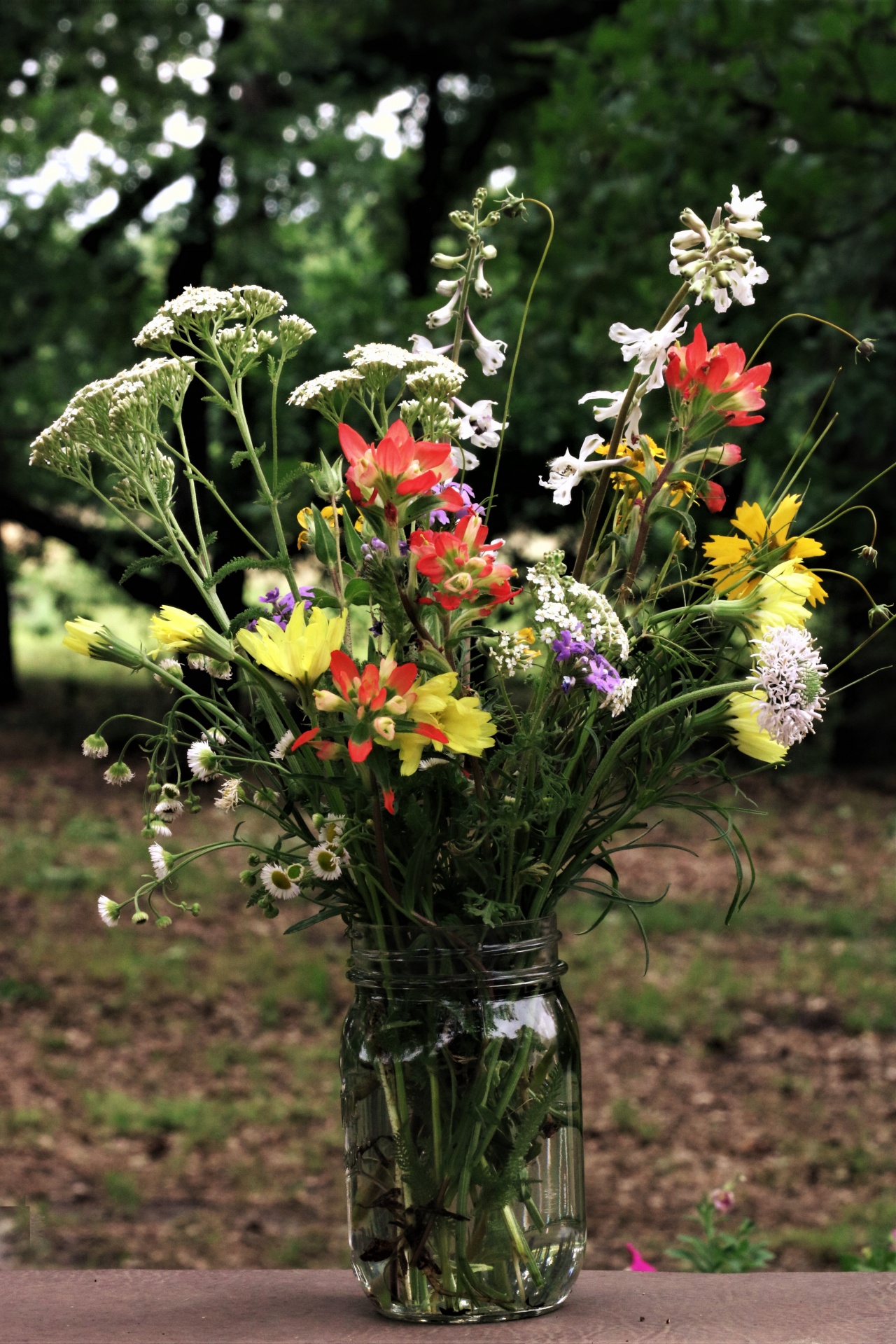 Close-up of various wildflowers in a jar sitting outside on a picnic table.