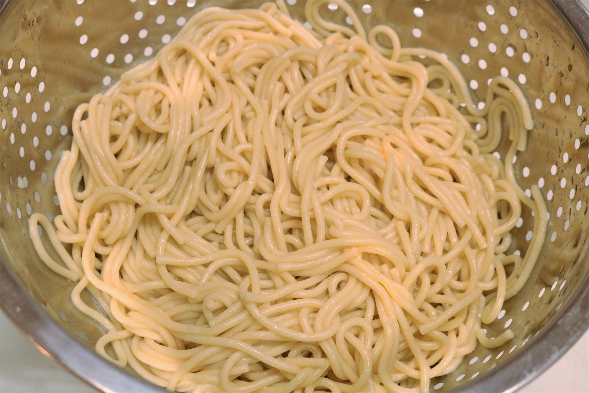 Cooked spaghetti noodles in a metal colander, close-up.