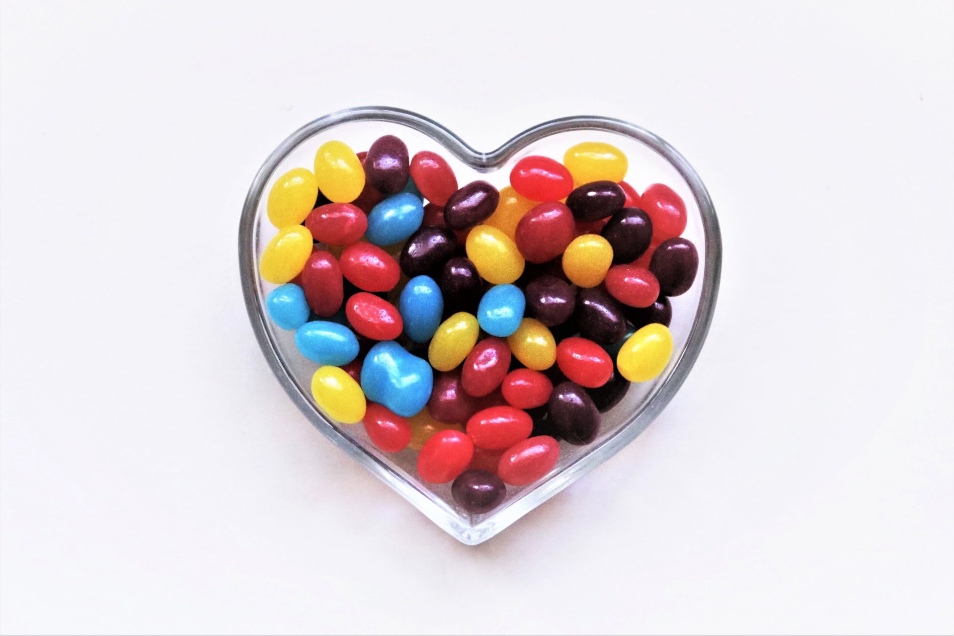 A clear glass heart shaped dish full of colorful jelly beans.