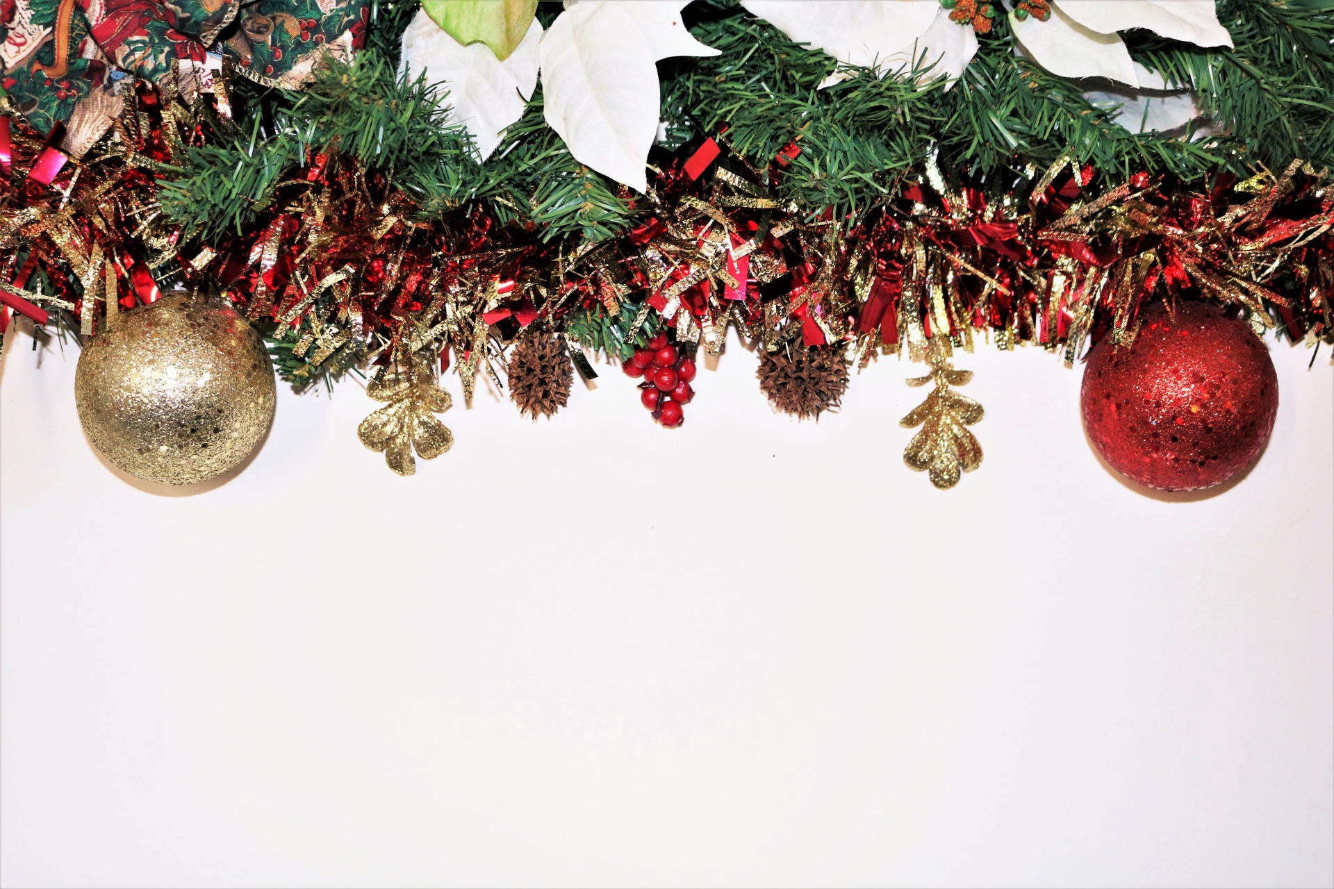 Colorful Christmas tinsel and red and gold ornaments frame the top of a white background with copy space.