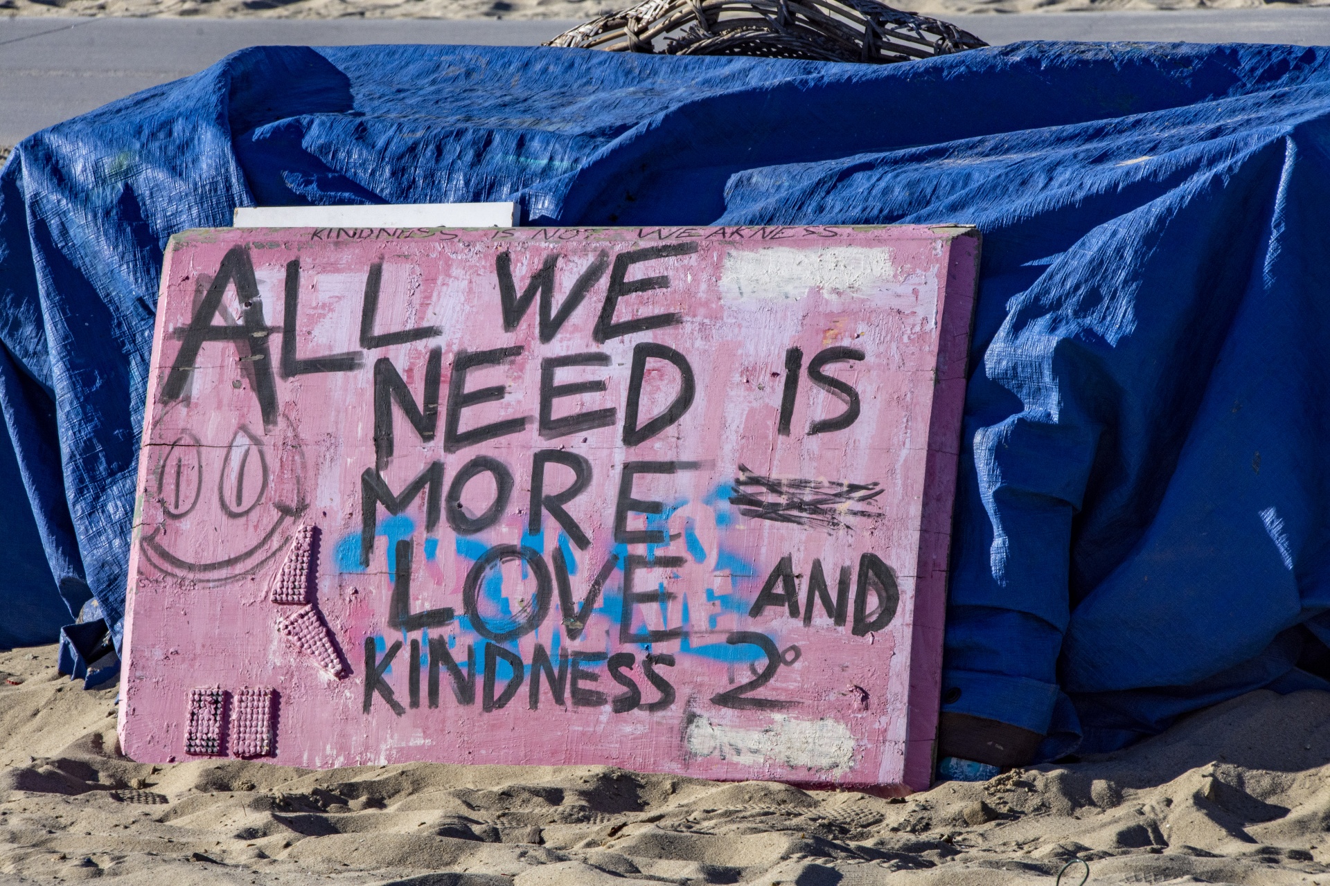 all we need is more love and kindness. sign painted and resting against a homeless tent