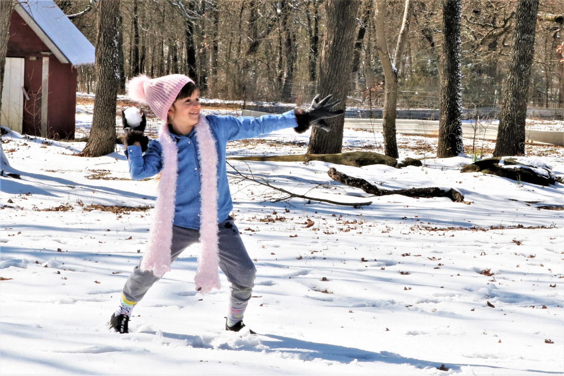 A cute little girl is standing in the snow, throwing a snowball.