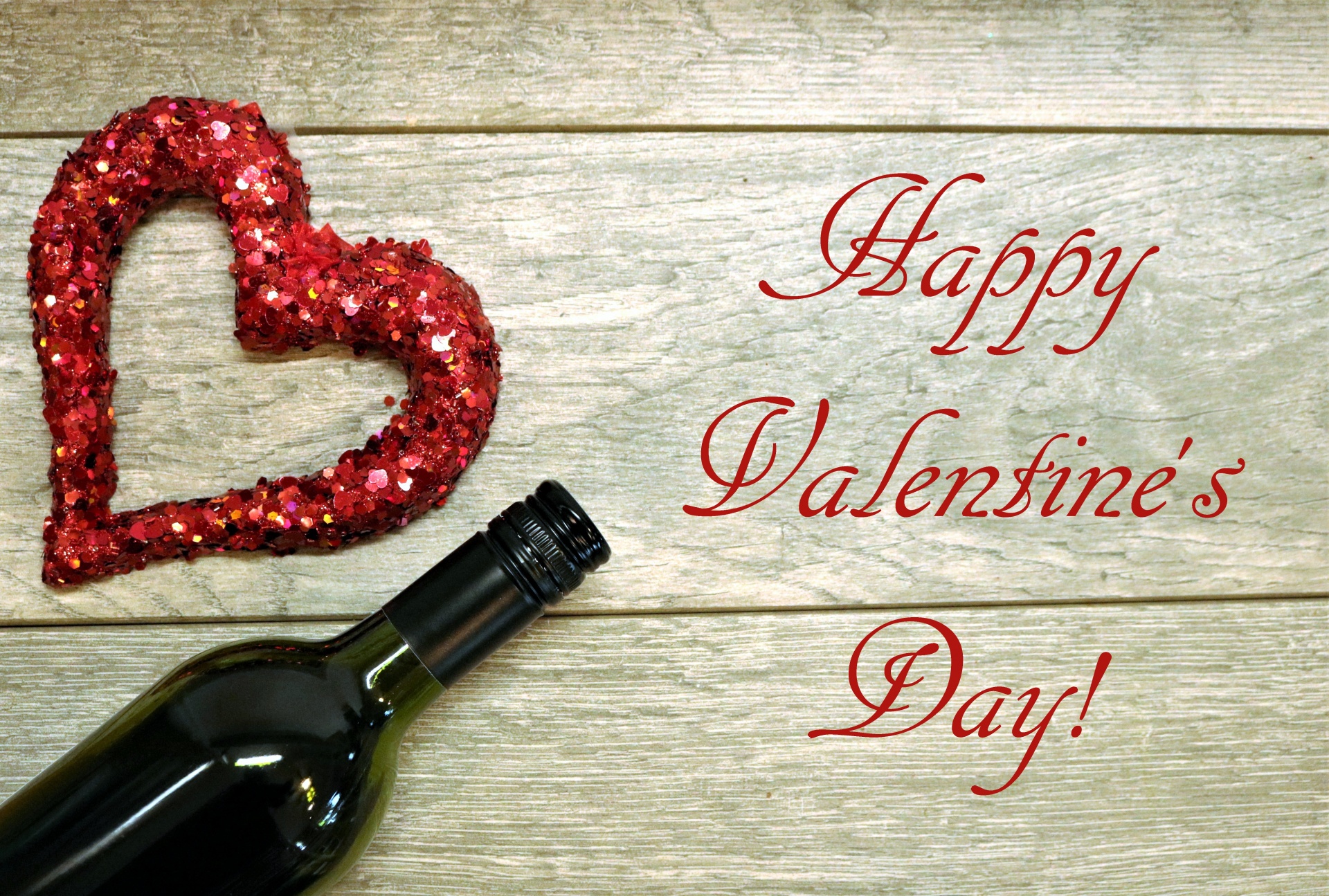 A red glitter heart and a wine bottle border the left side of a wood grain background, with text, Happy Valentine's Day.