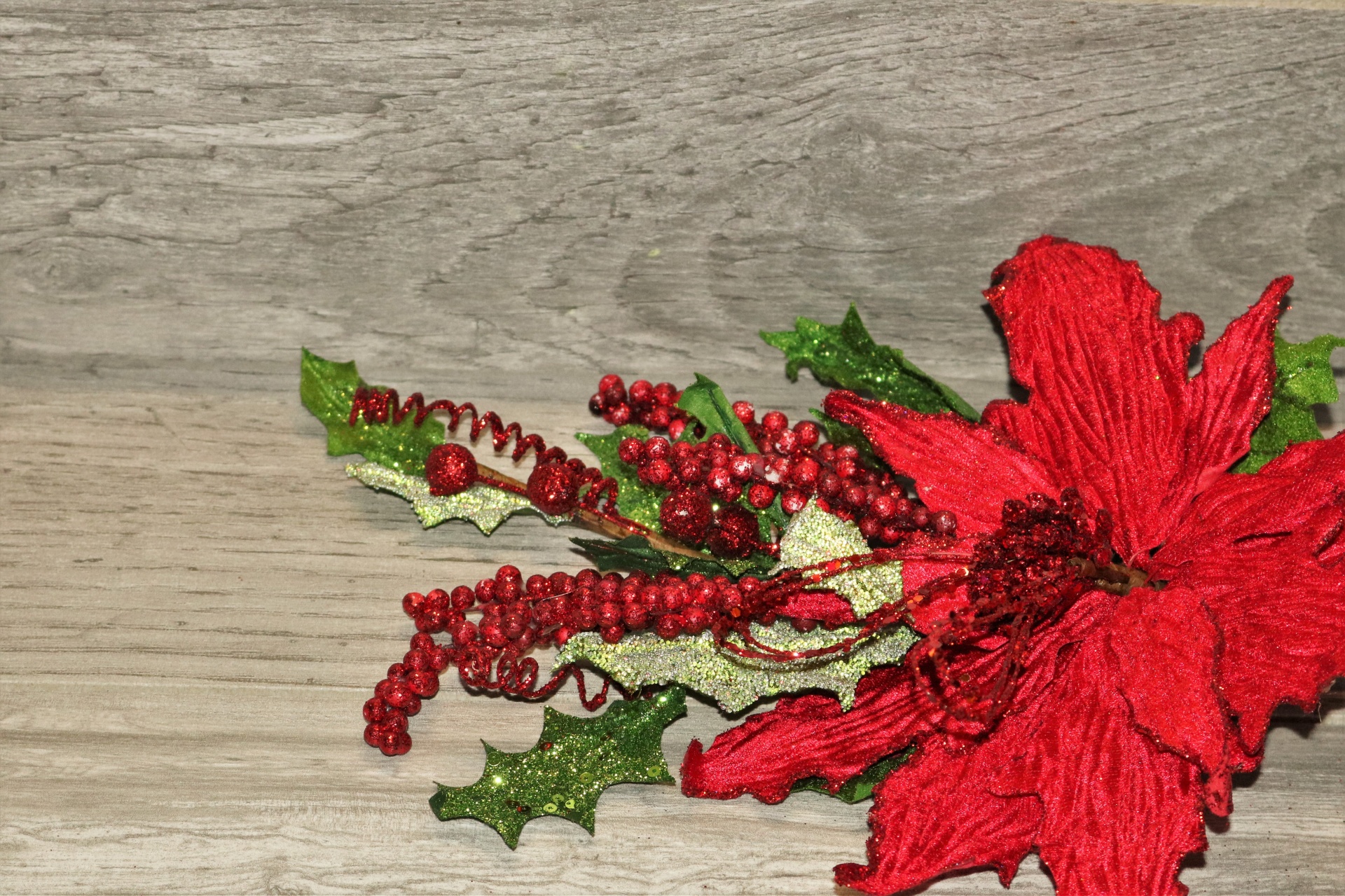 Close-up of a sparkling red poinsettia flower, with green holly leaves and red berries, on a wood background with copy space.