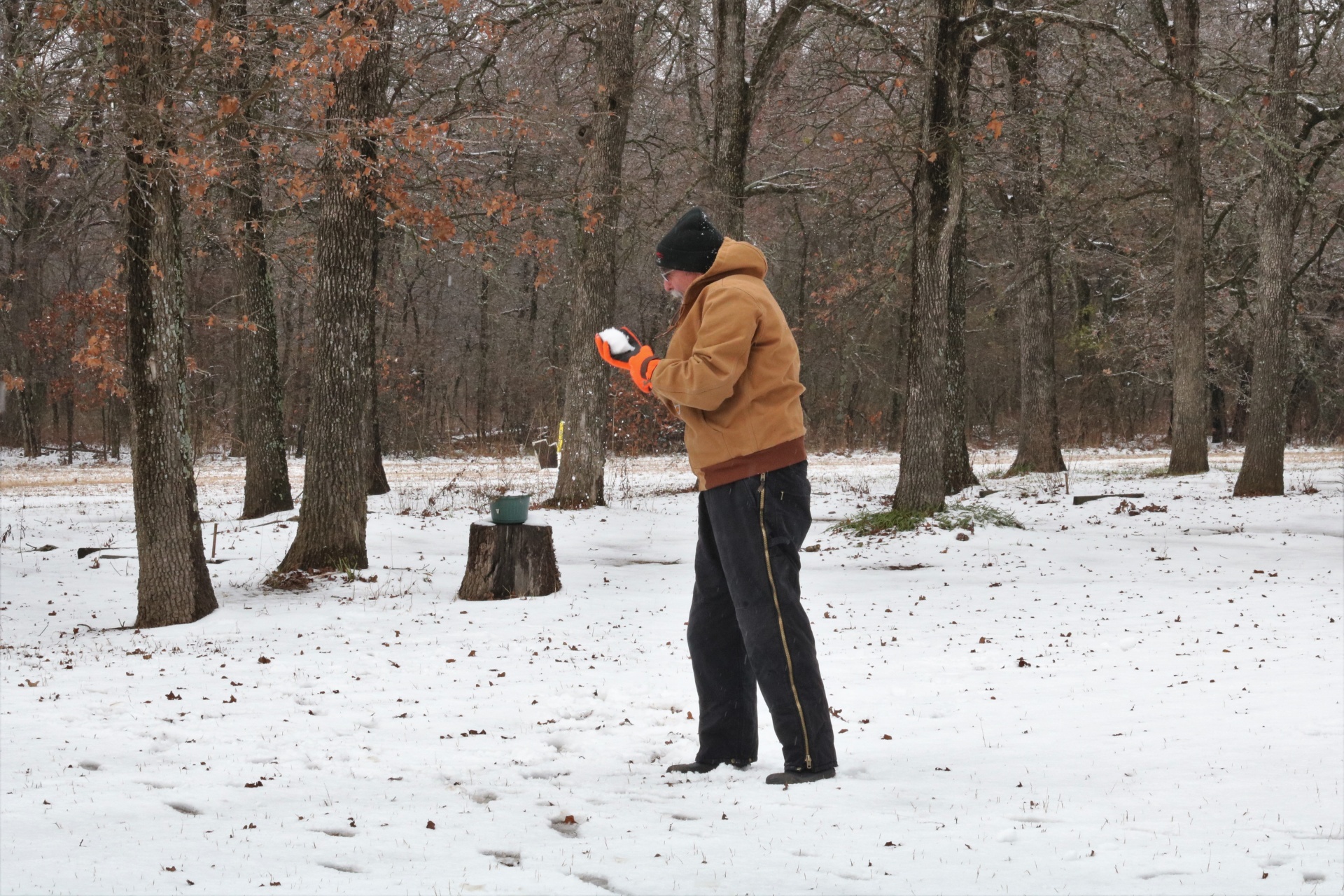 A senior man, in the woods, making a snowball.