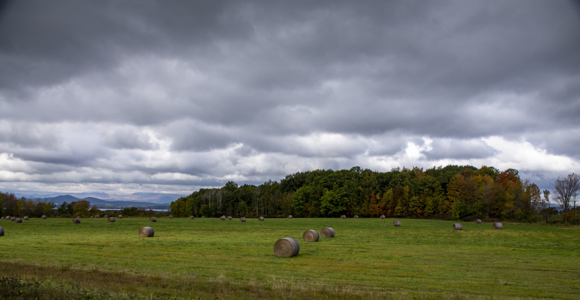 bales of hay on a grassy field underneath cloudy dark sky