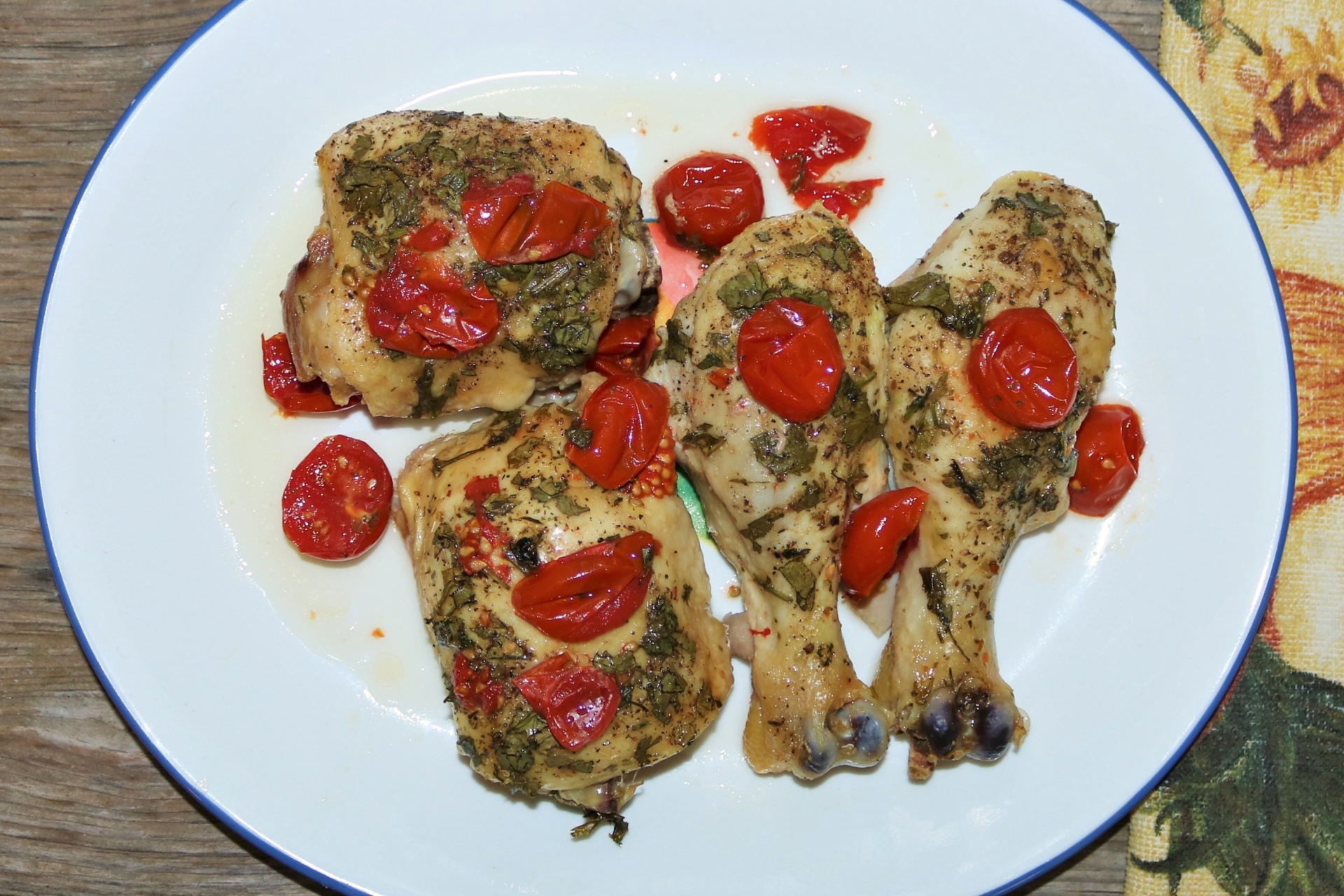 Top view of cooked chicken pieces with cherry tomatoes and spices on a white plate.