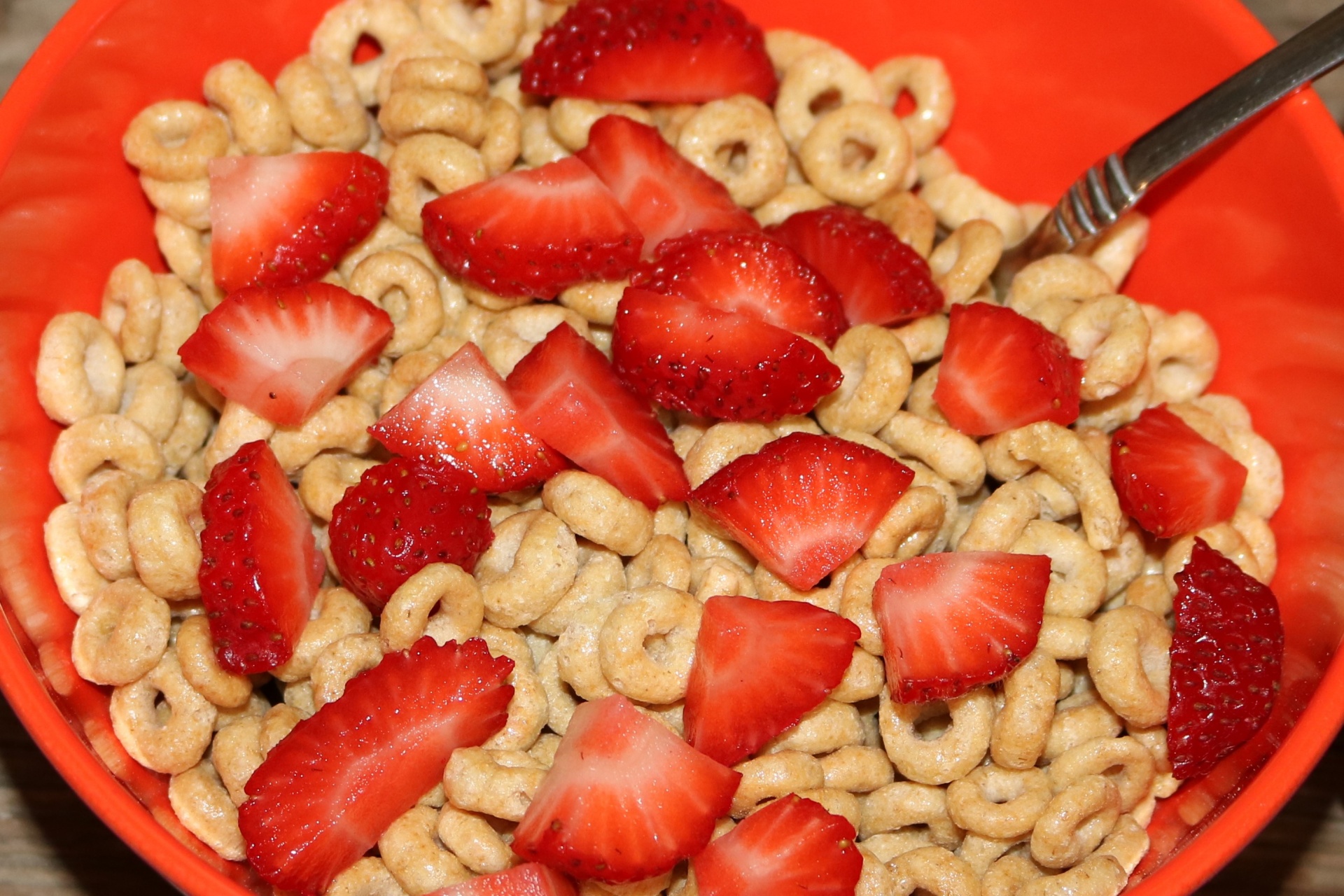 Close-up top view of a red bowl filled with oat cereal and sliced red strawberries.