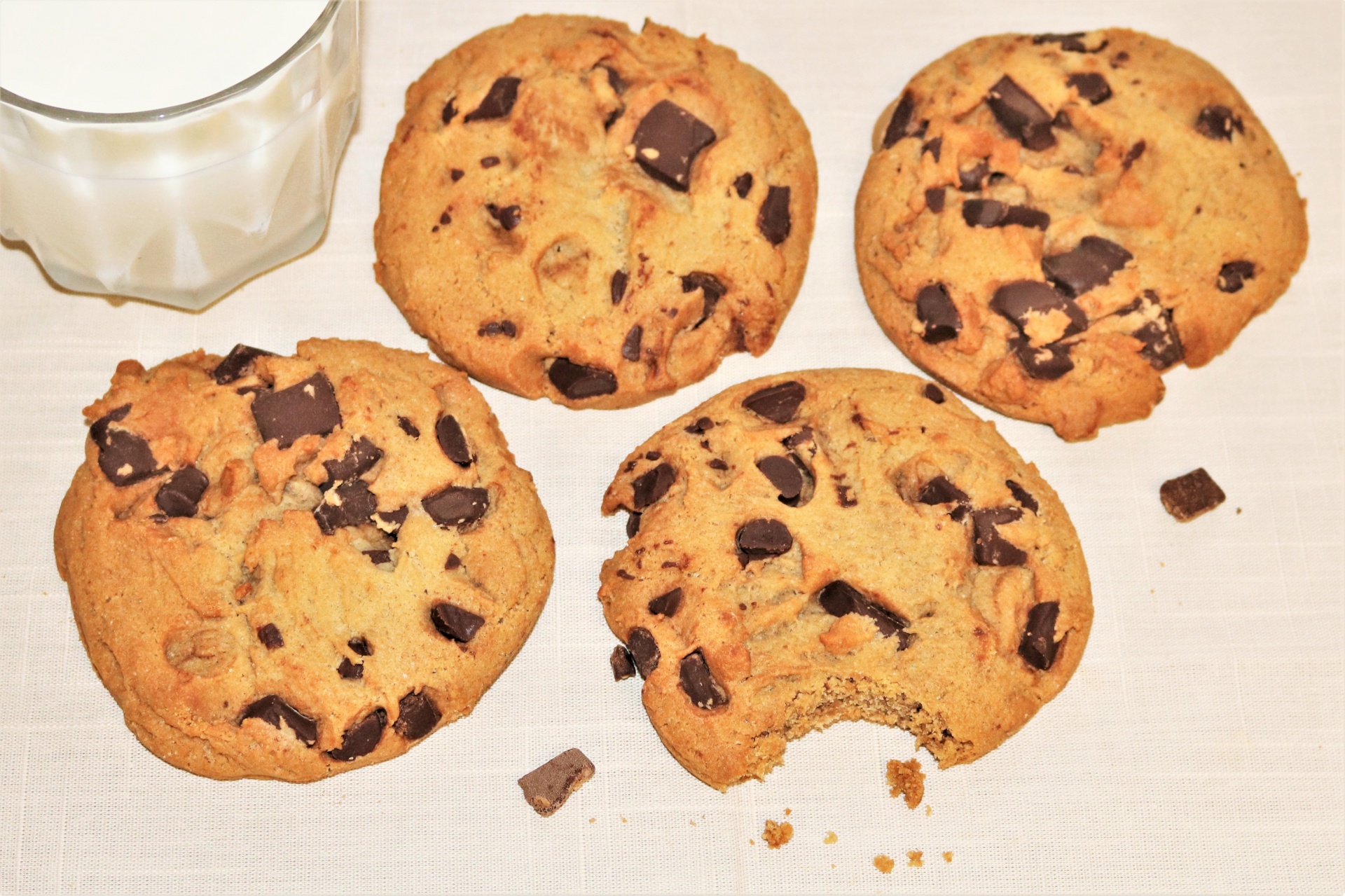 Four chocolate chip cookies and a glass of milk on a white table.